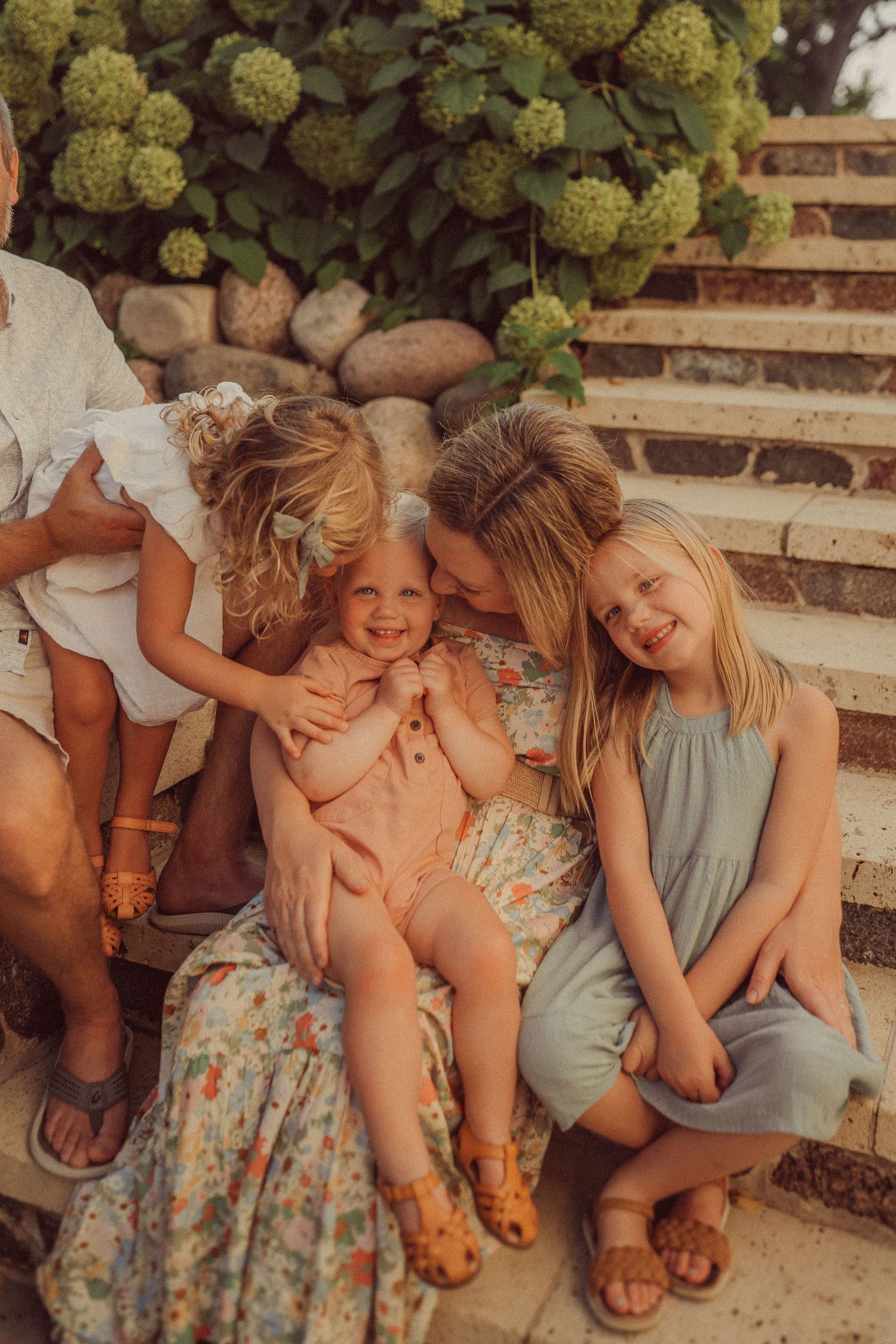 Candid family moment captured on stone steps with blooming hydrangeas in warm summer light.