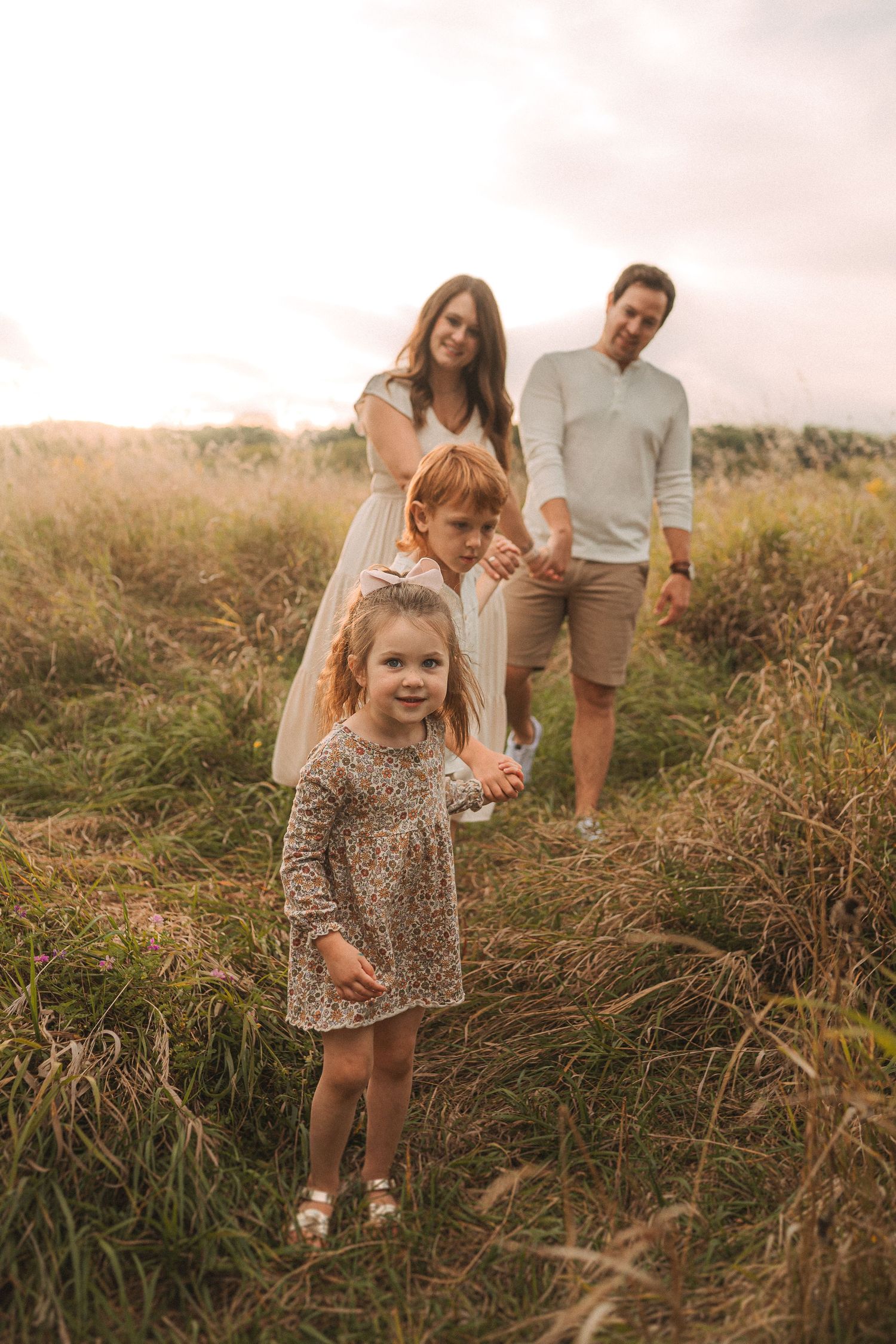 Family stands together in tall grass during sunset with warm golden lighting.