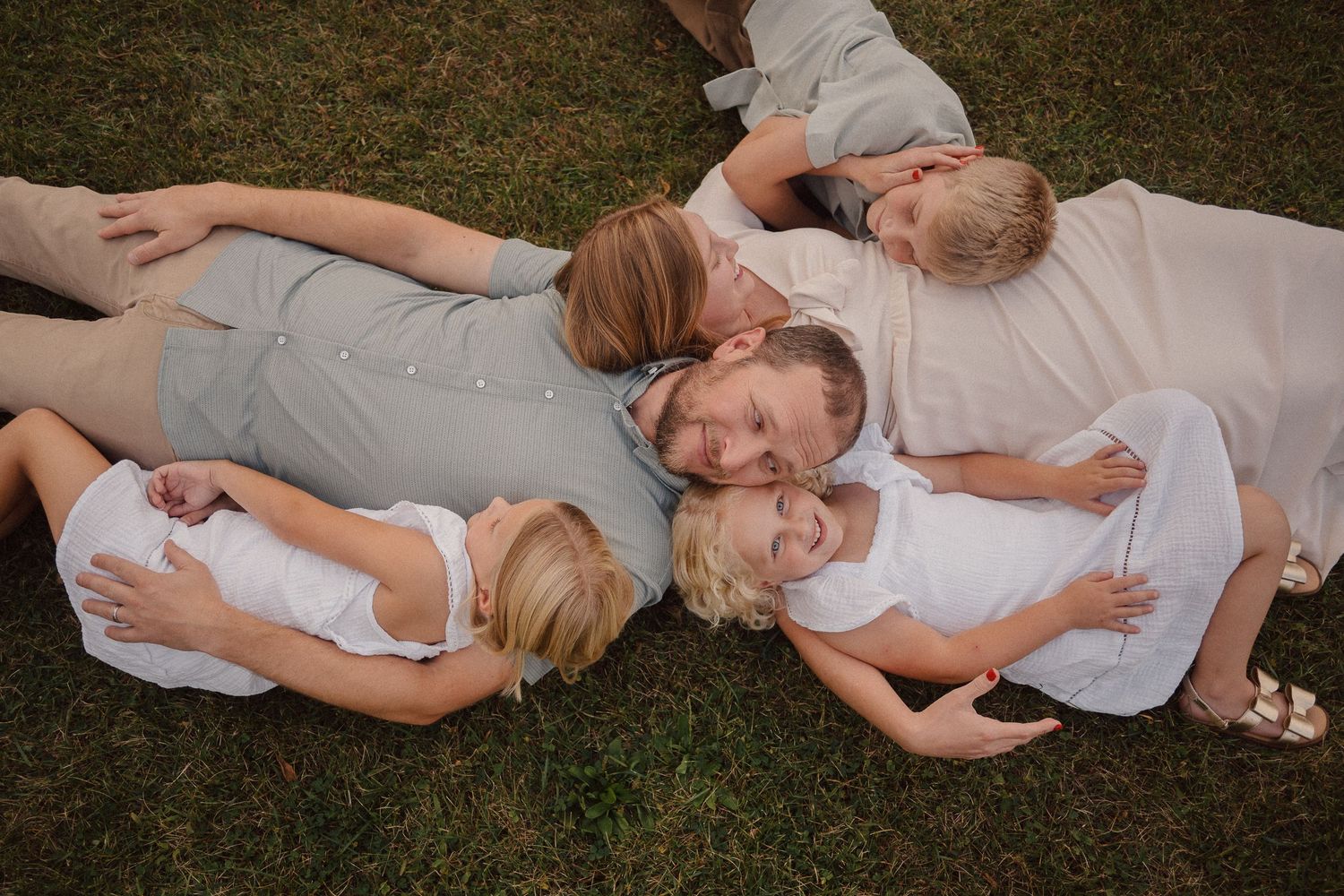 Family members lying down together on grass in coordinated white and gray outfits.