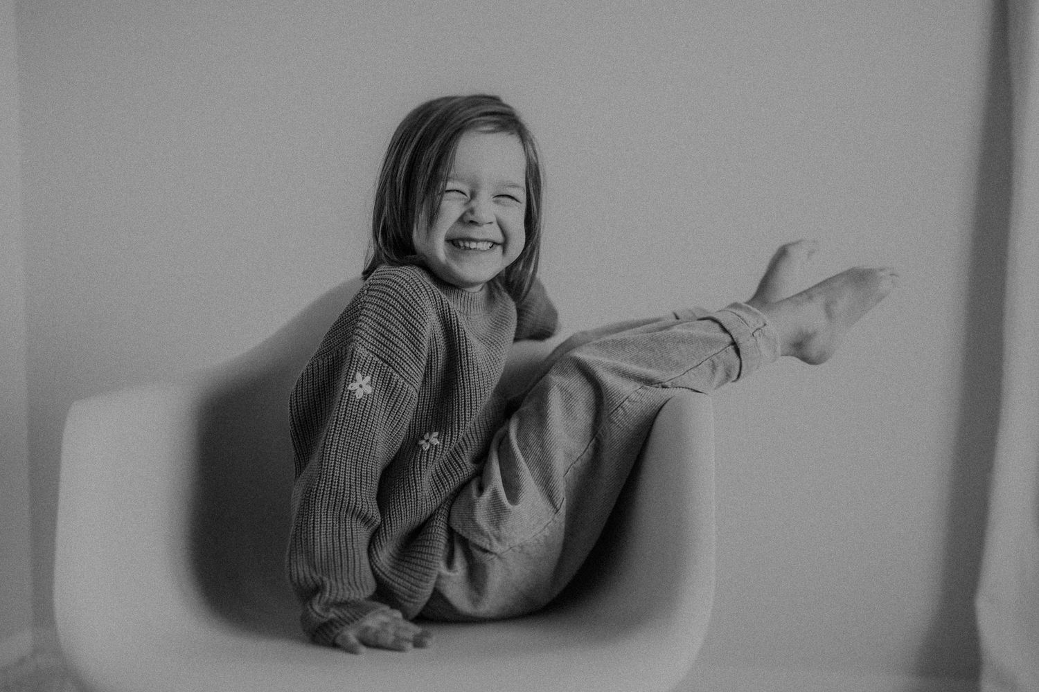 A playful child lying in a gray sweater poses joyfully against a white background.