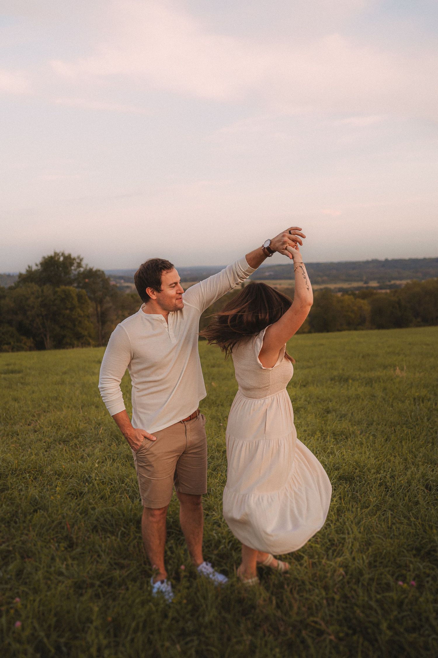 Two people dance playfully in a rolling meadow at sunset.