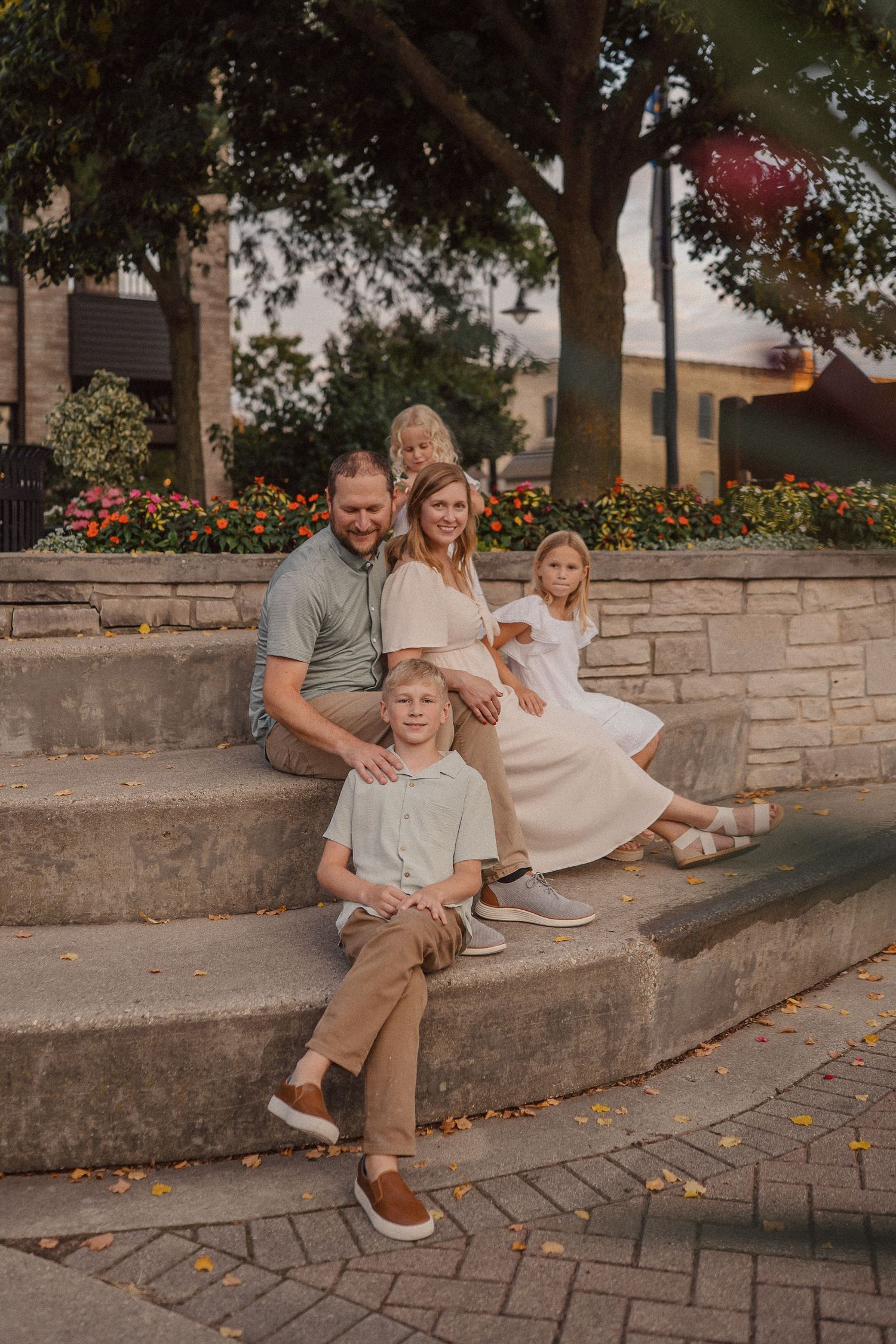 Family group relaxing together on curved stone steps surrounded by autumn trees and flowers.
