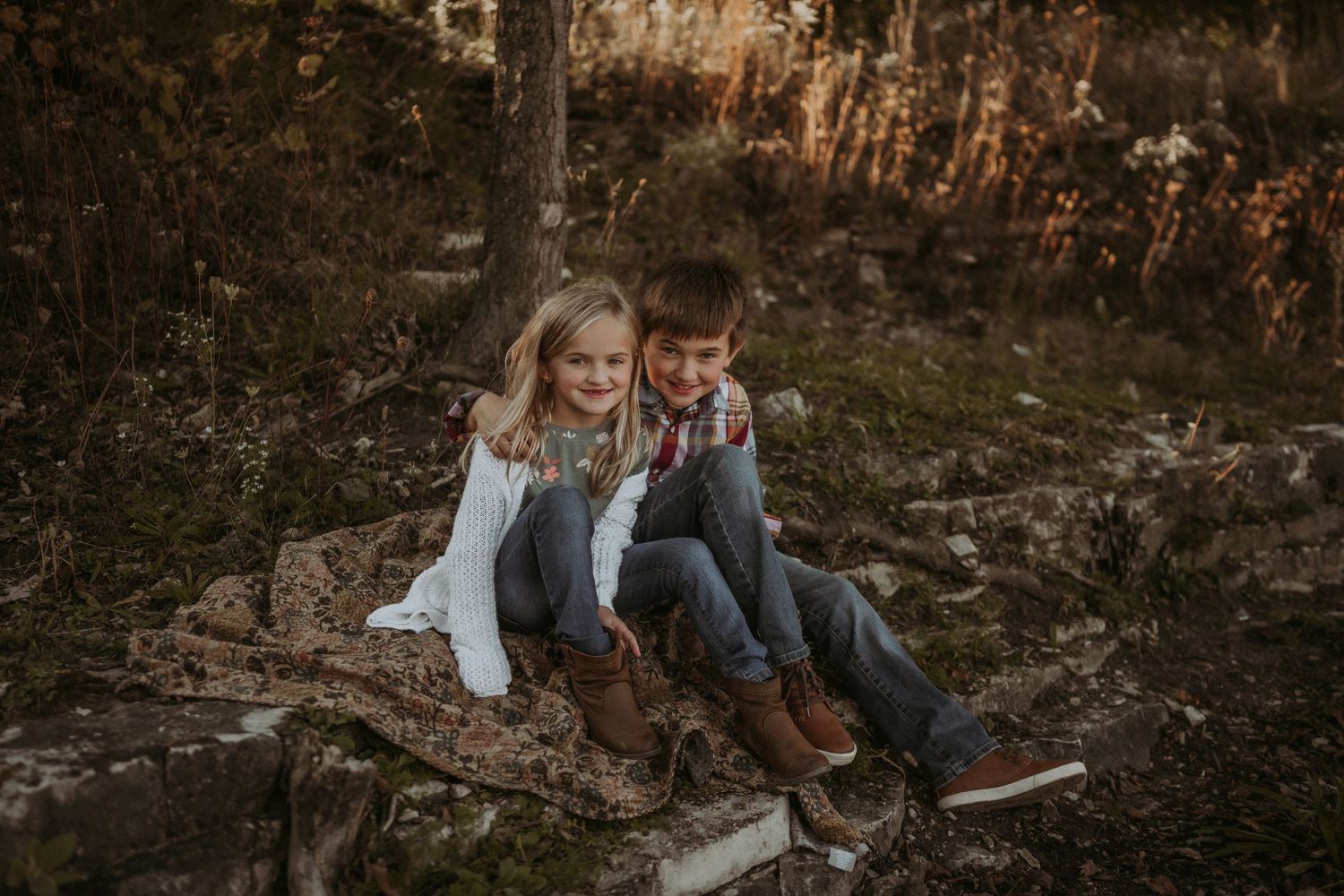 Two children sitting together on rocky steps in an autumn forest setting.