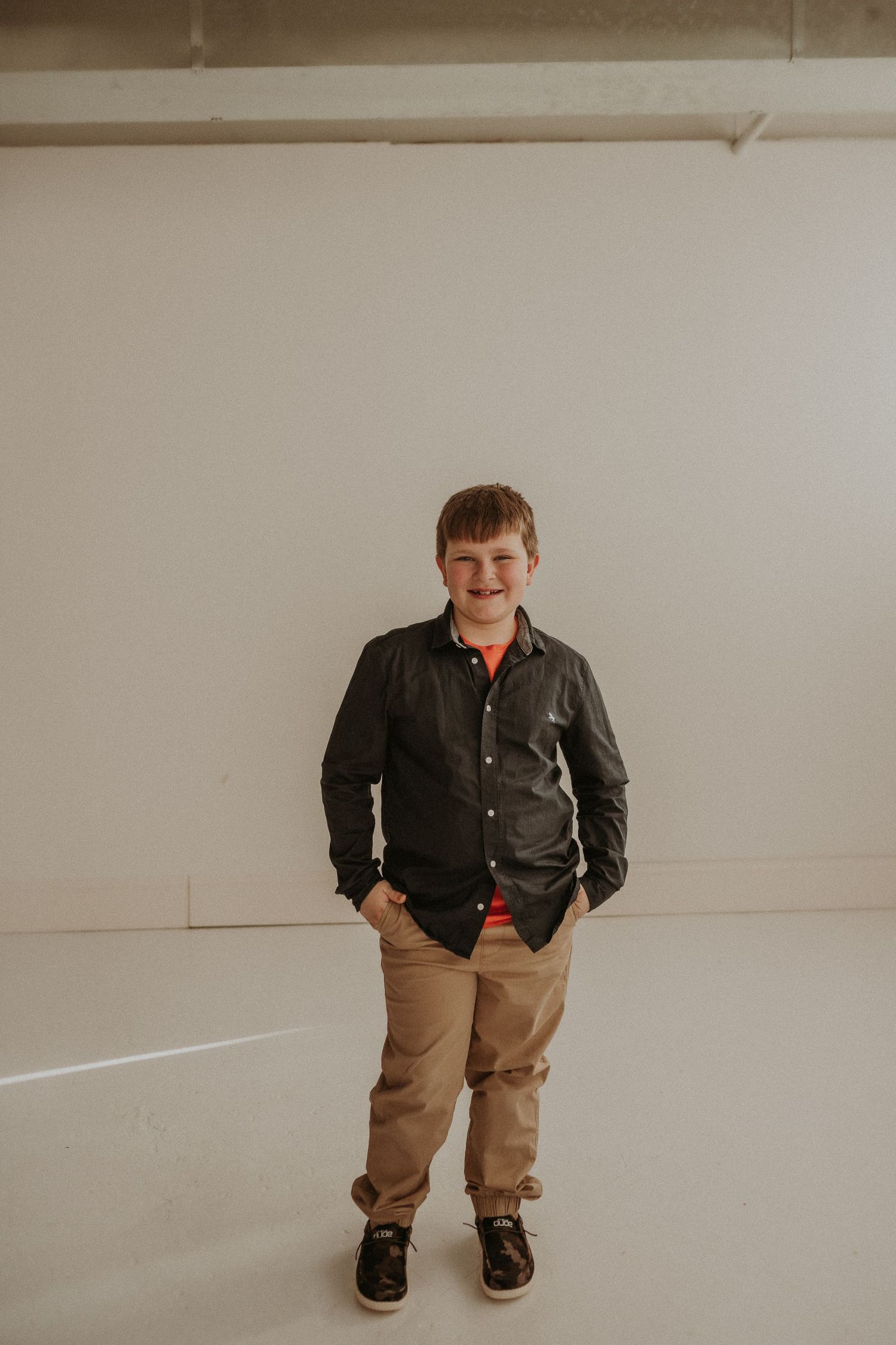 A full-length portrait showing someone in casual attire standing against a white studio backdrop.