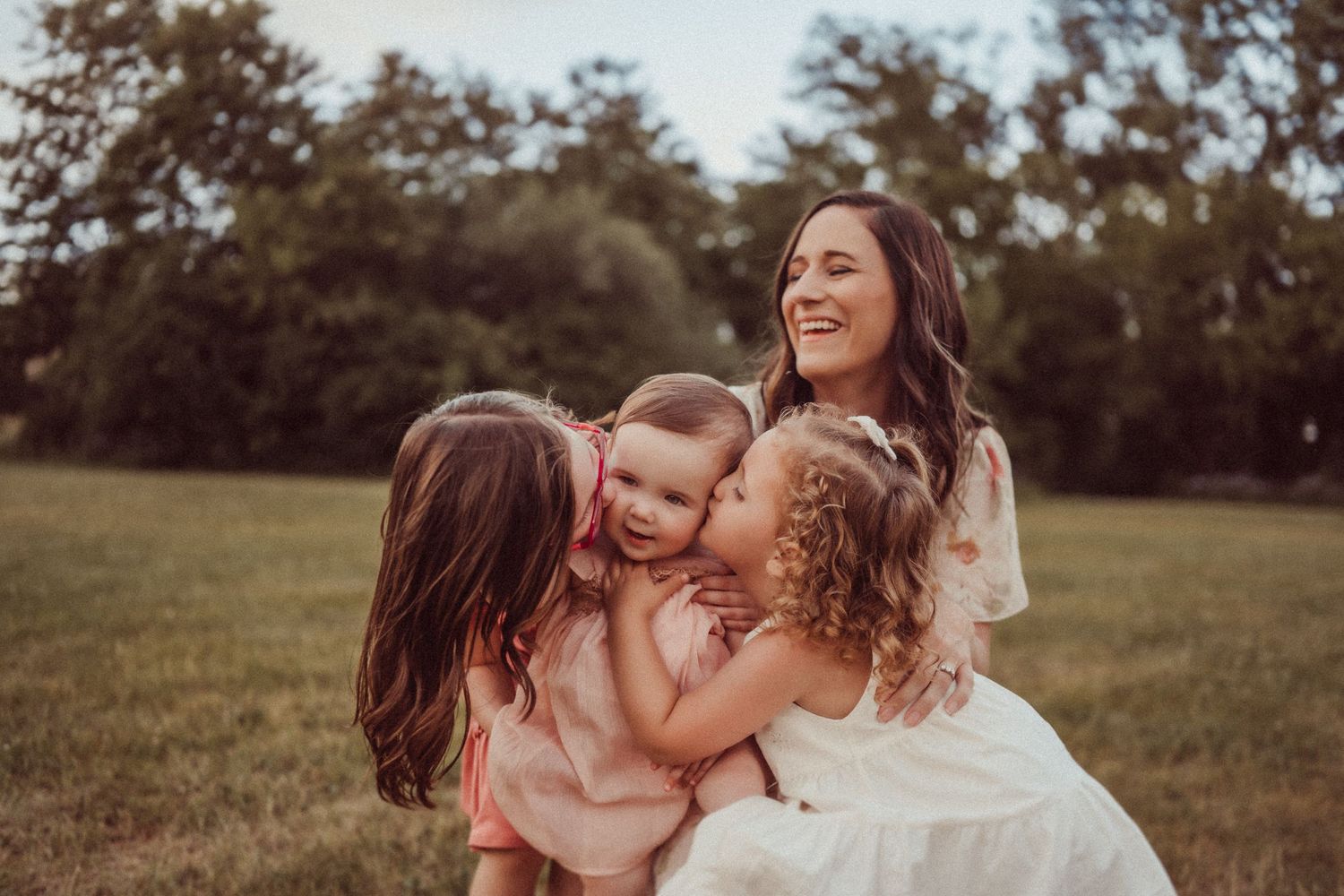 A joyful family moment captured in warm sunlight as they embrace and laugh together in a grassy field.