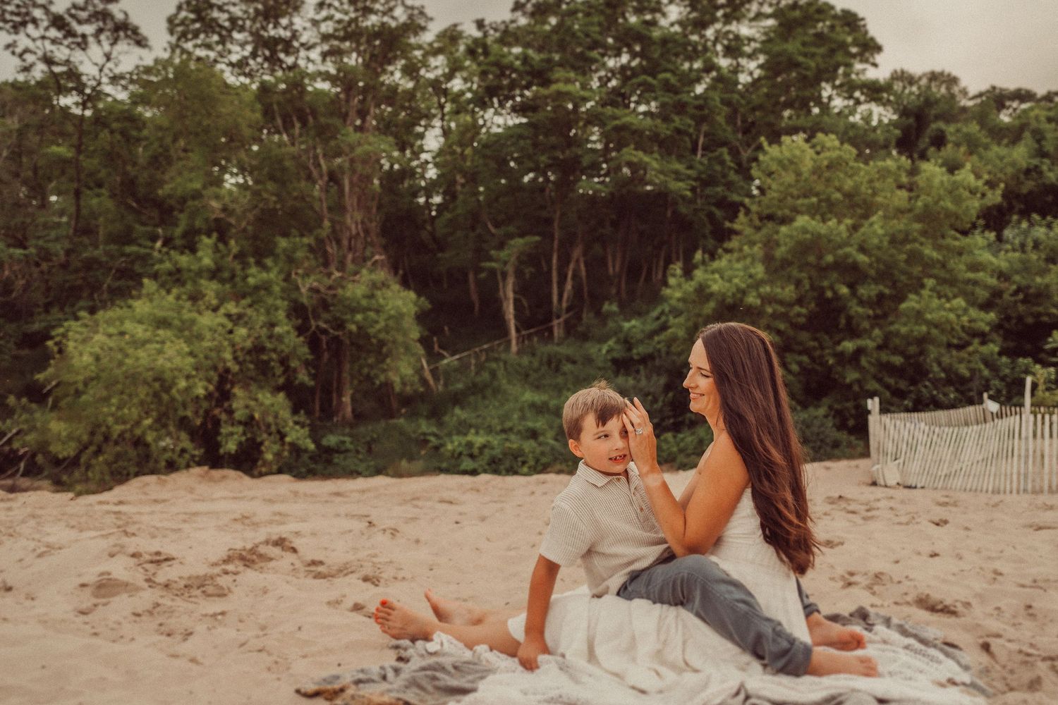 Two people share a playful moment while relaxing on a blanket at a sandy beach.