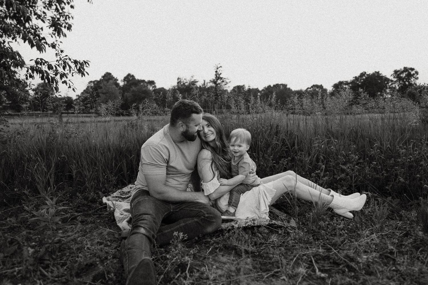 Black and white portrait of a family sitting together in tall grass.
