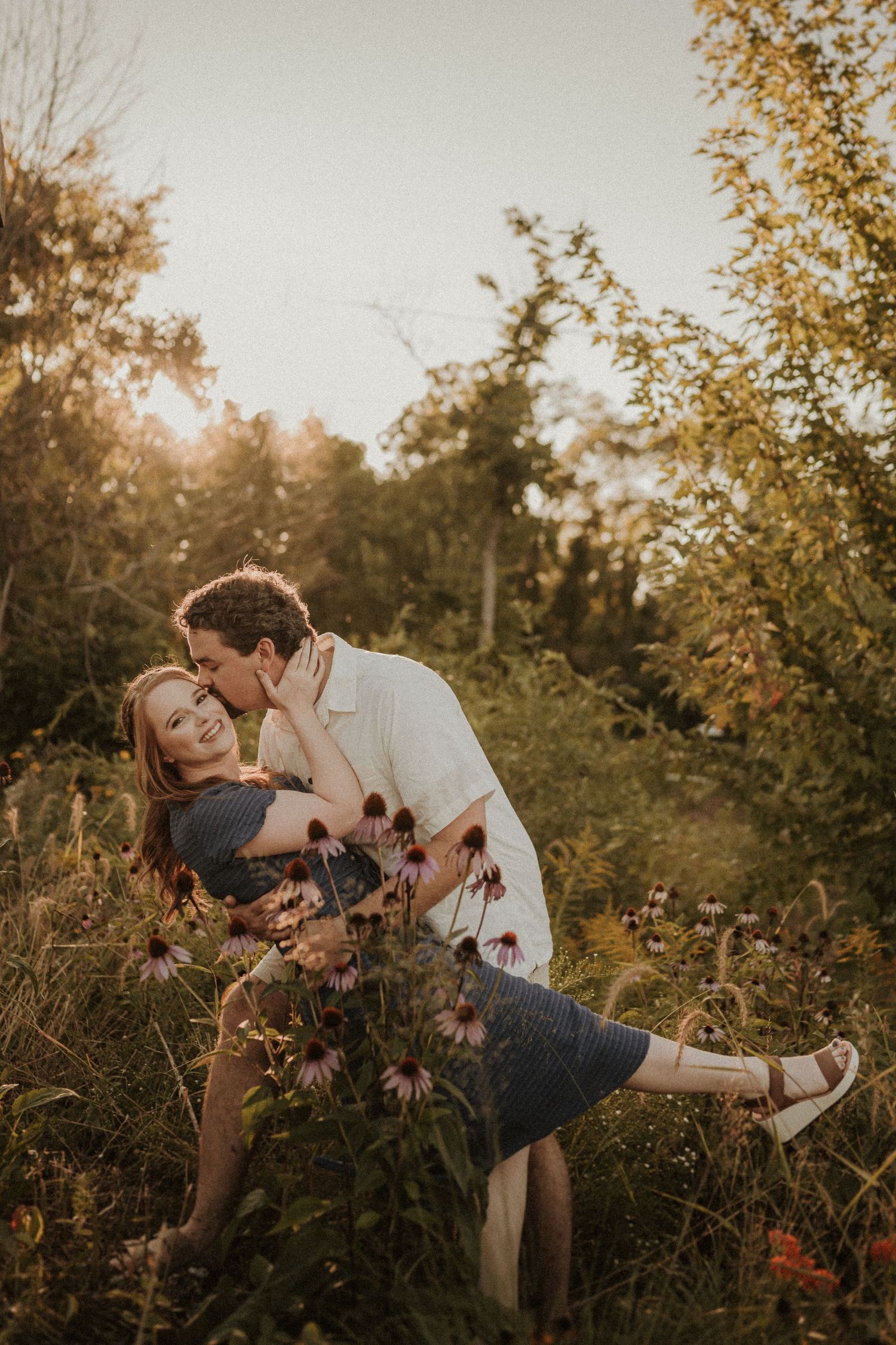 Couple sharing a romantic dip kiss among wildflowers at golden hour.