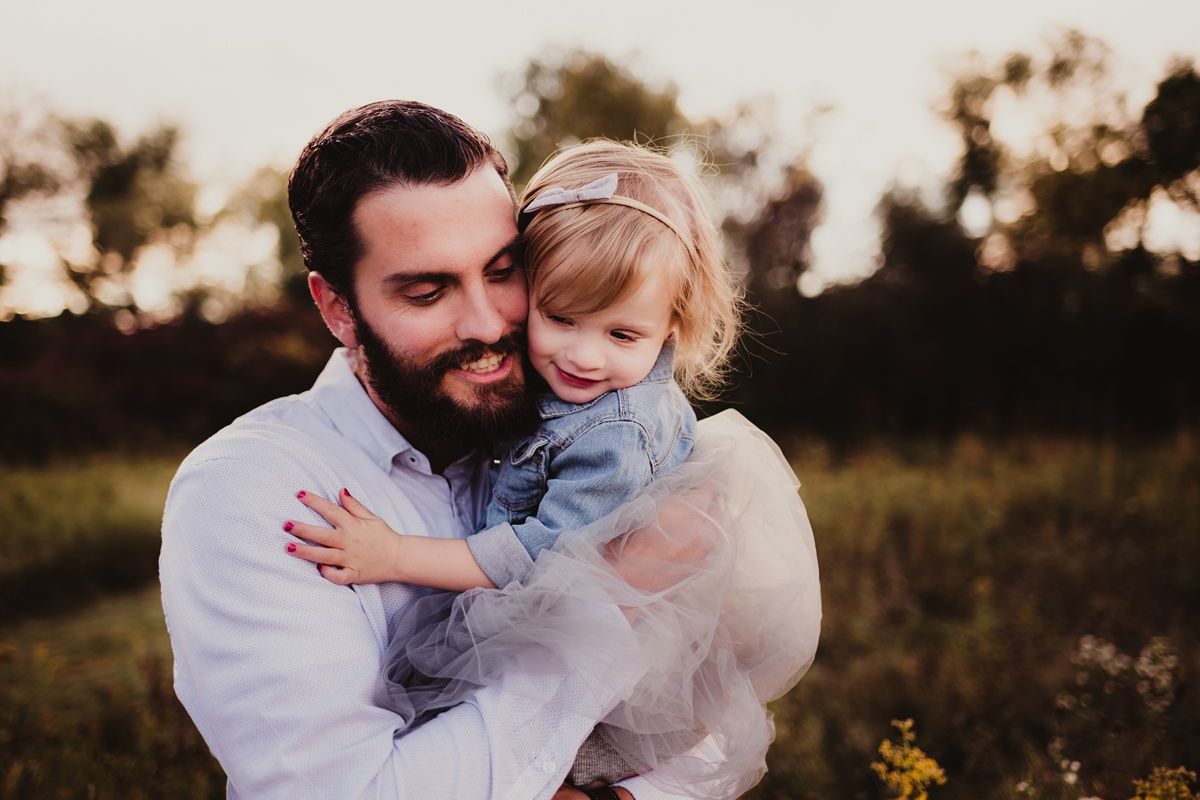 Candid sunset scene of parent and child sharing a warm embrace in a field.