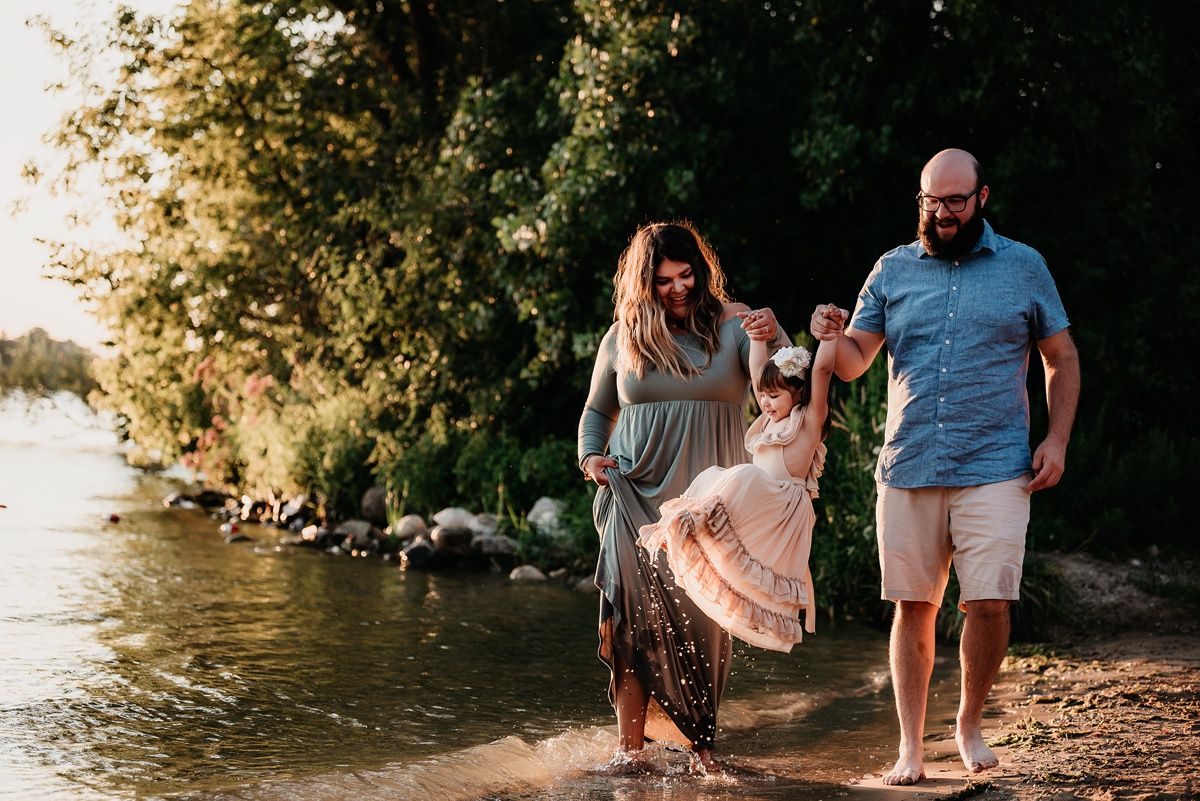 Family enjoying sunset stroll along rocky shoreline with golden light filtering through trees.