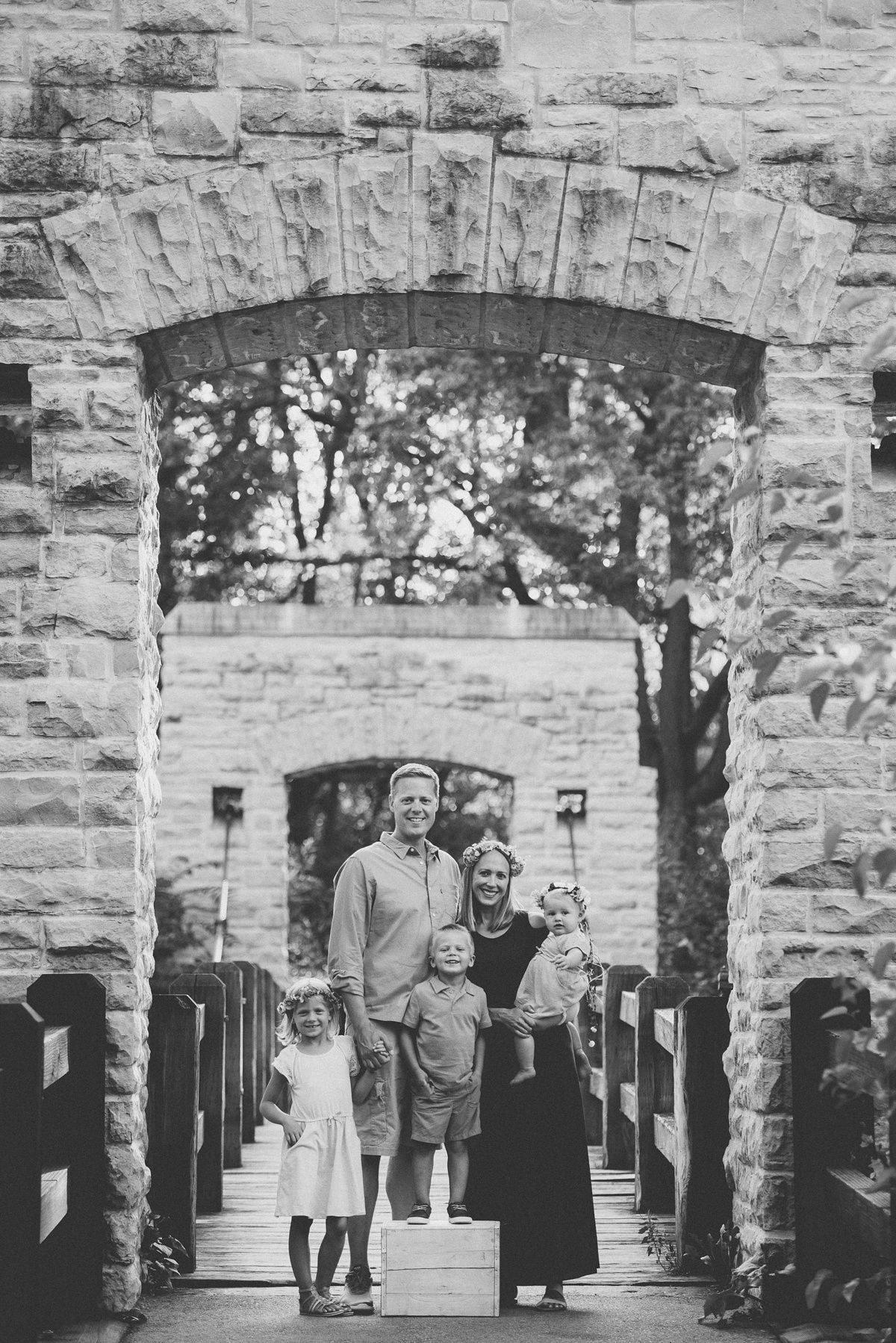 Black and white portrait of family standing in historic stone archway.