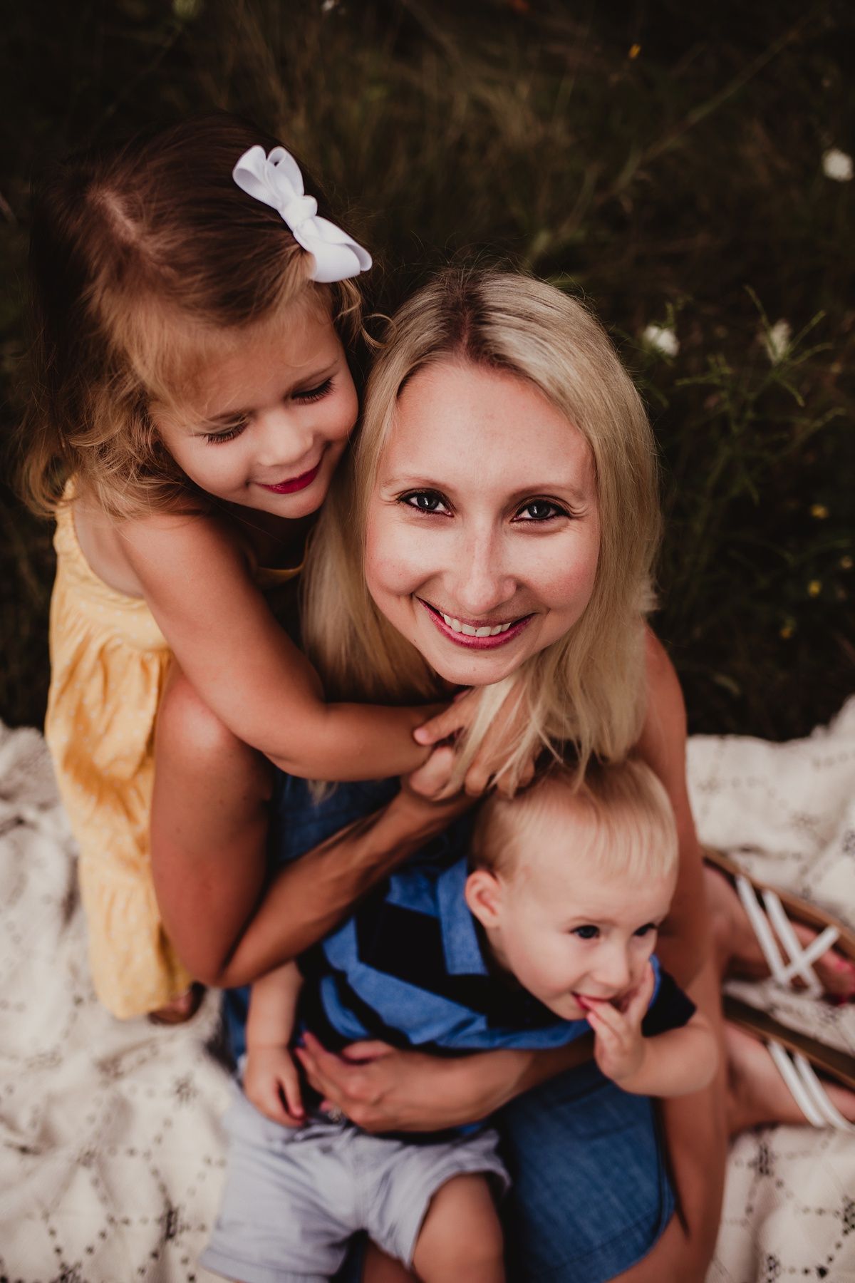 Candid family portrait outdoors with everyone smiling and embracing on a blanket.