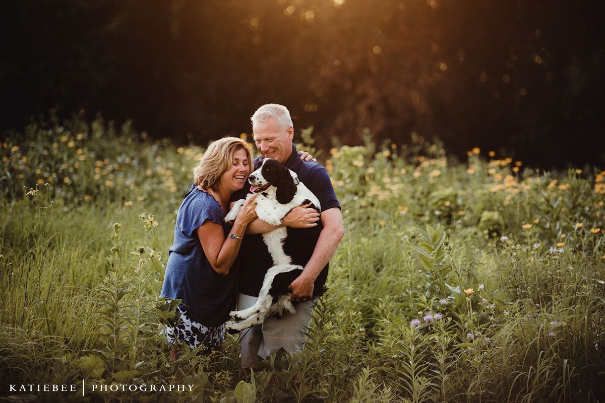 Couple kneels together in golden evening light among wildflowers and tall grass.