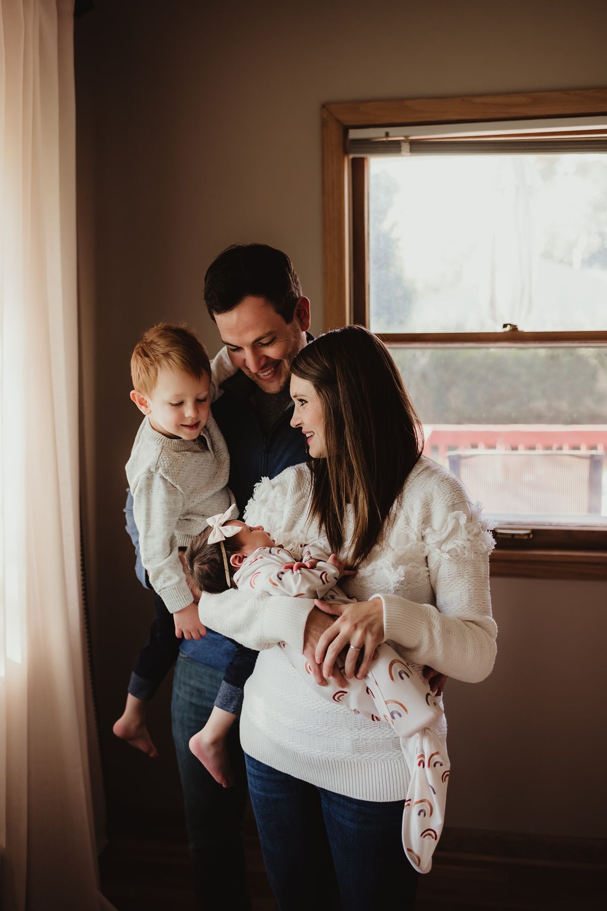 Candid family moment with parents and children by a sunny window.