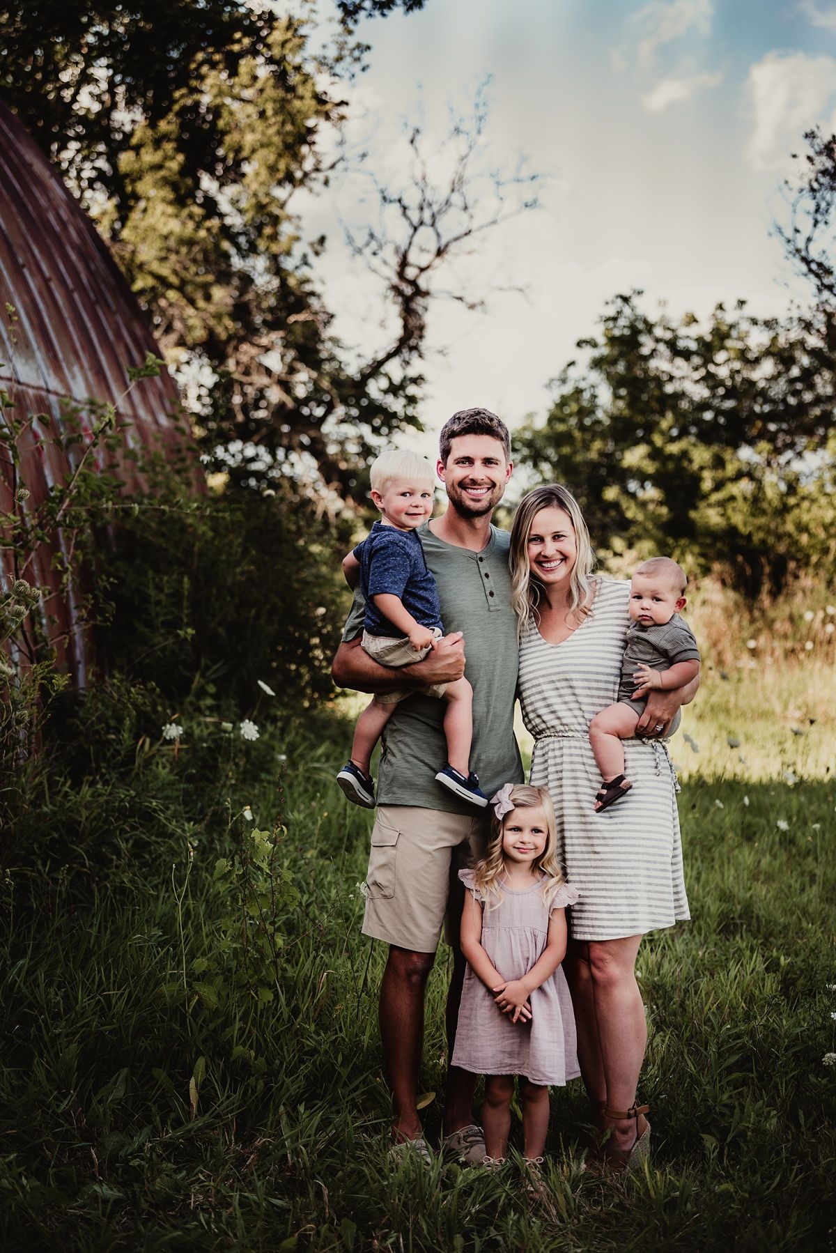 A family poses together in front of a rustic barn on a sunny summer evening.