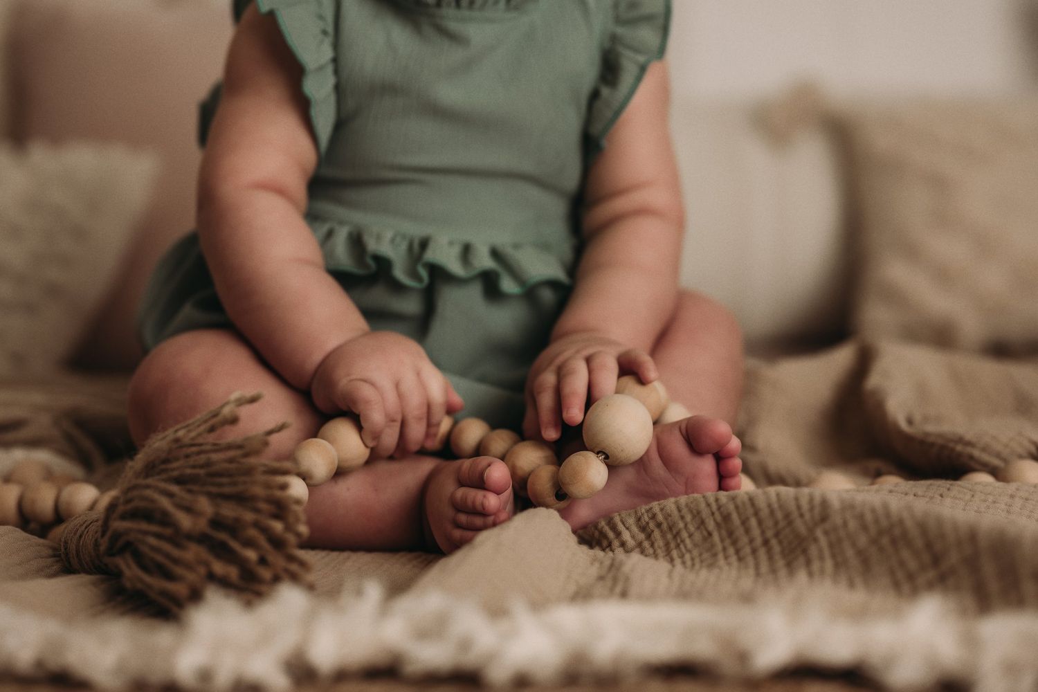 Close-up of tiny feet and hands on a textured blanket with wooden beads.