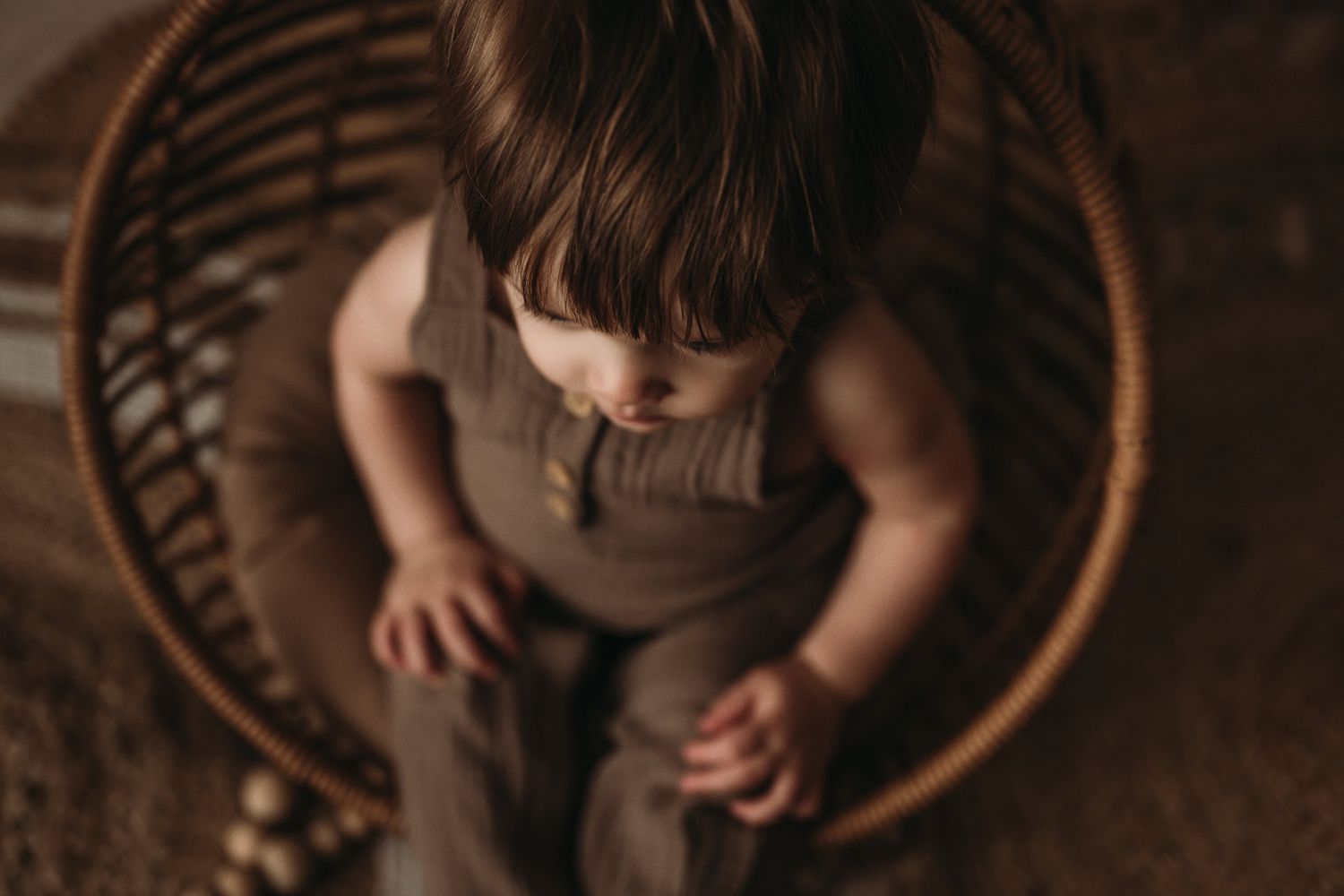 Top view of a small child seated in a round rattan chair against a neutral backdrop.