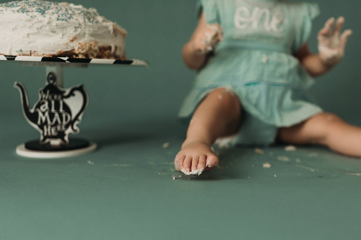 Close-up view of bare feet and dress hem next to an ornate cake stand with a white cake.