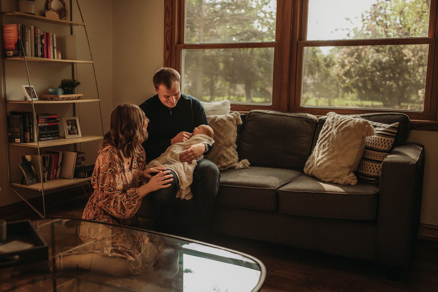 A family sharing tender moments with their newborn baby on a grey couch.