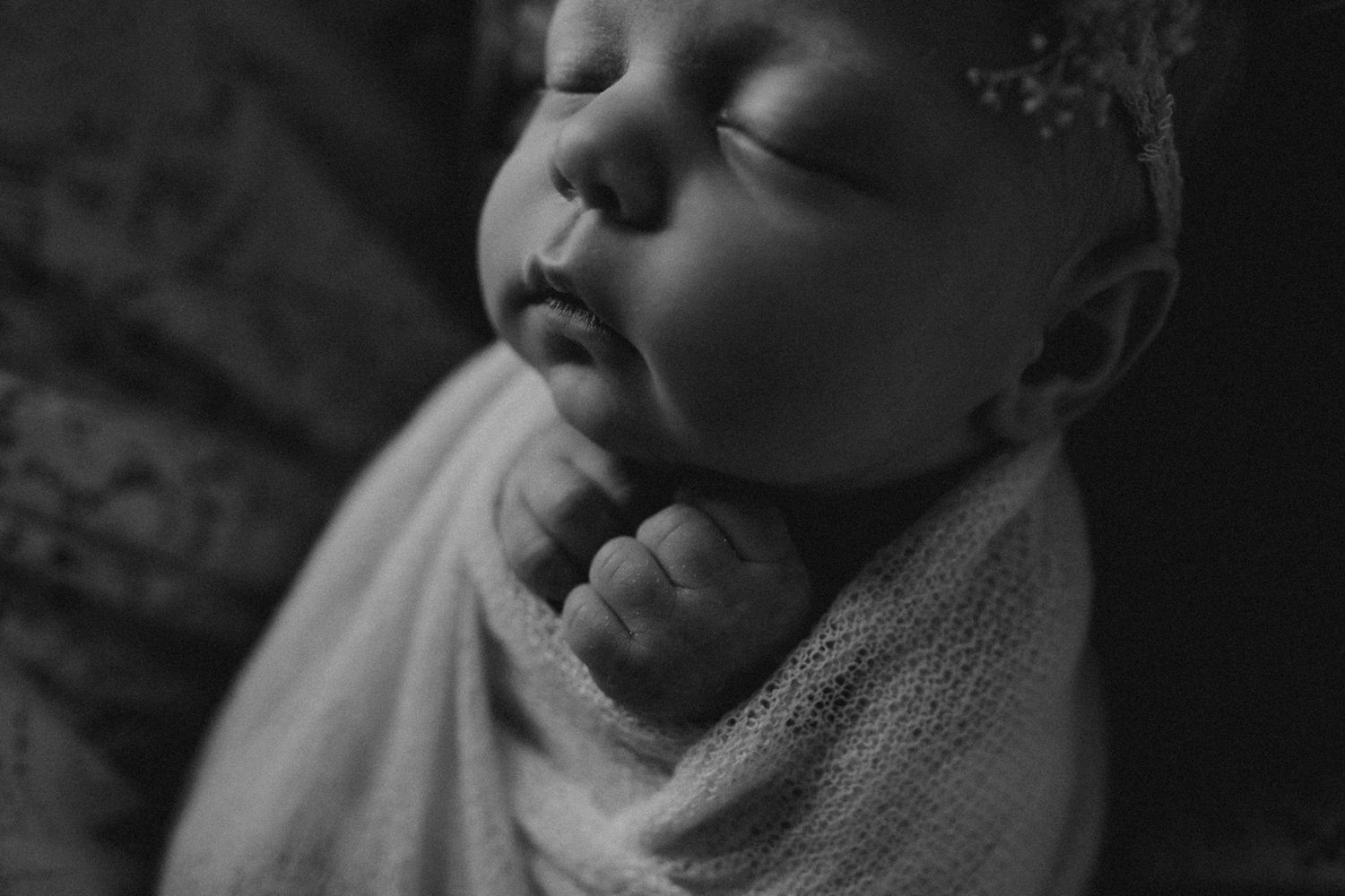 Black and white portrait of sleeping newborn swaddled in light fabric with lace headband.