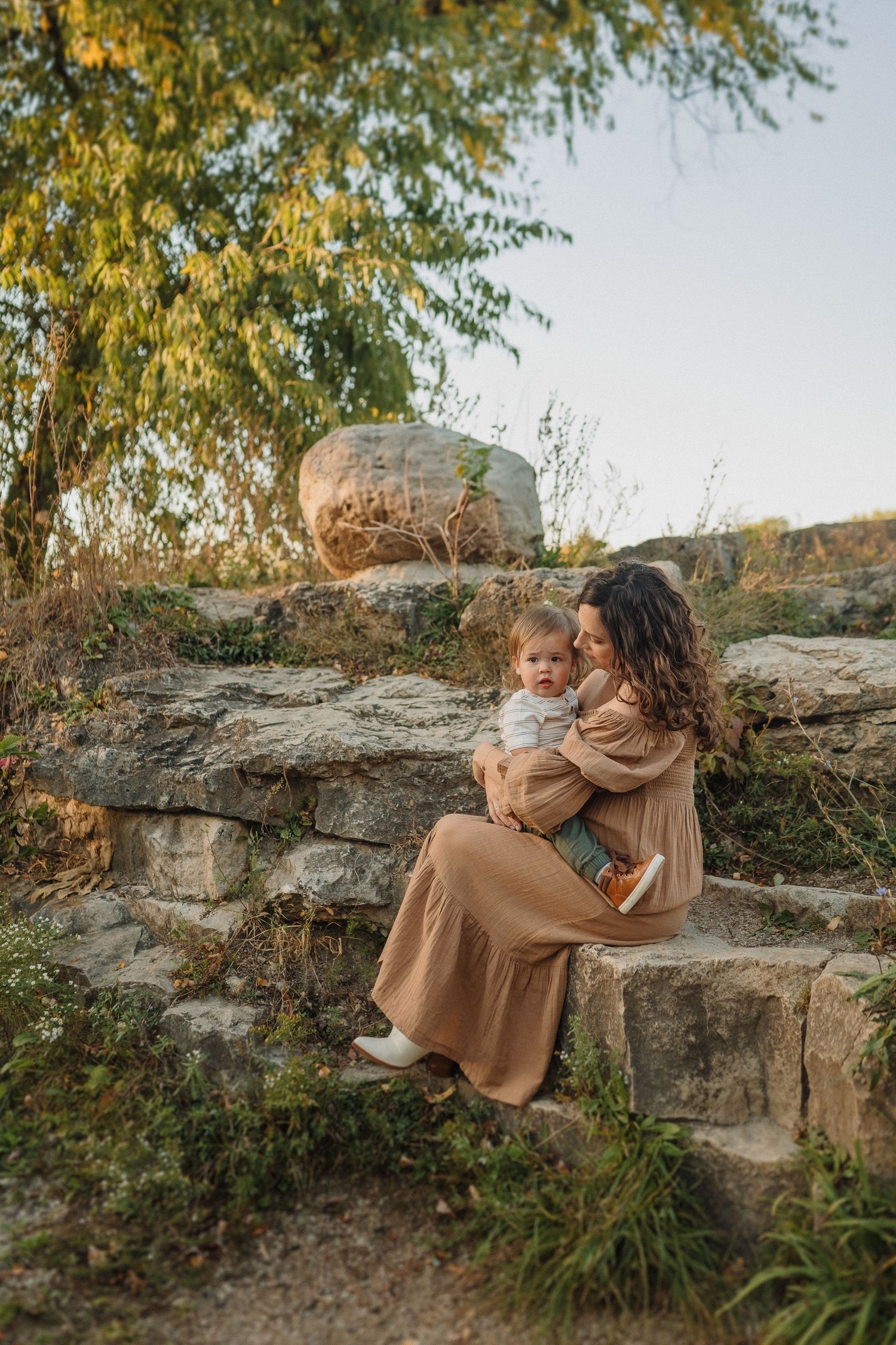 A tender moment captured on stone steps as a pair sits together against an autumn backdrop with golden foliage.