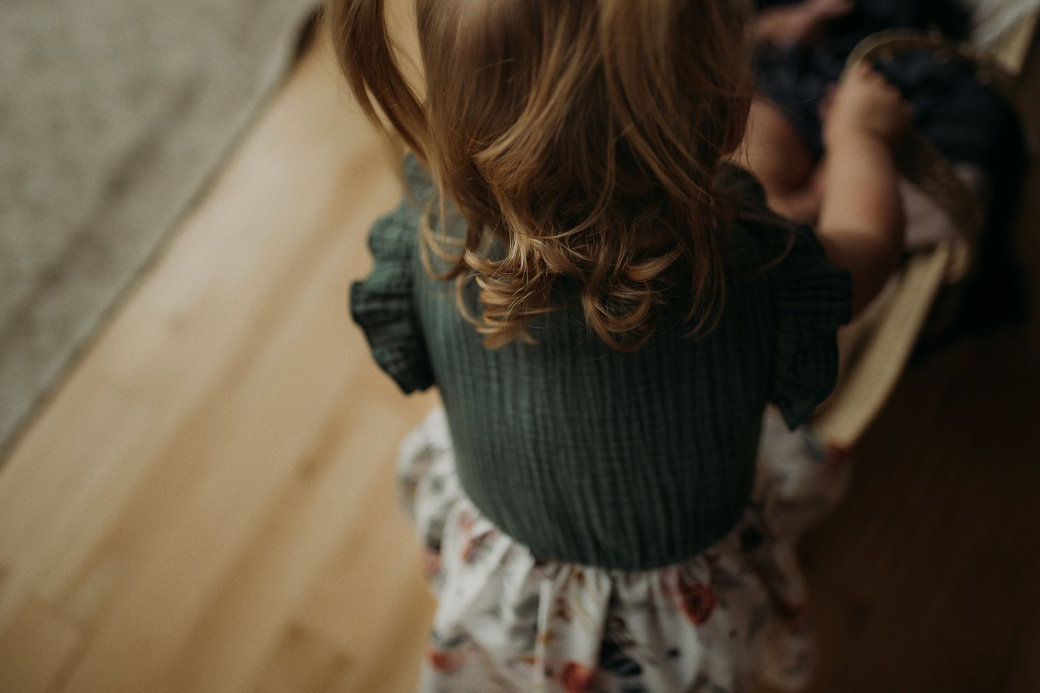 Back view of green sweater and floral dress on wooden floor.