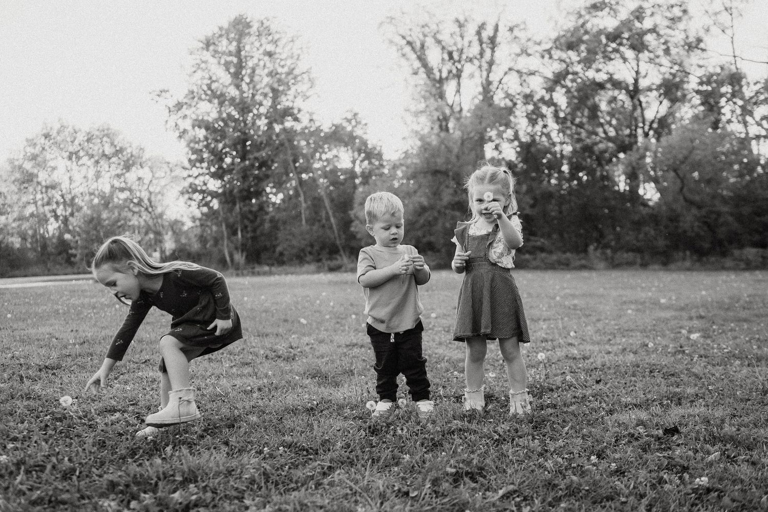 Black and white photo of children playing in a field with trees in the background.