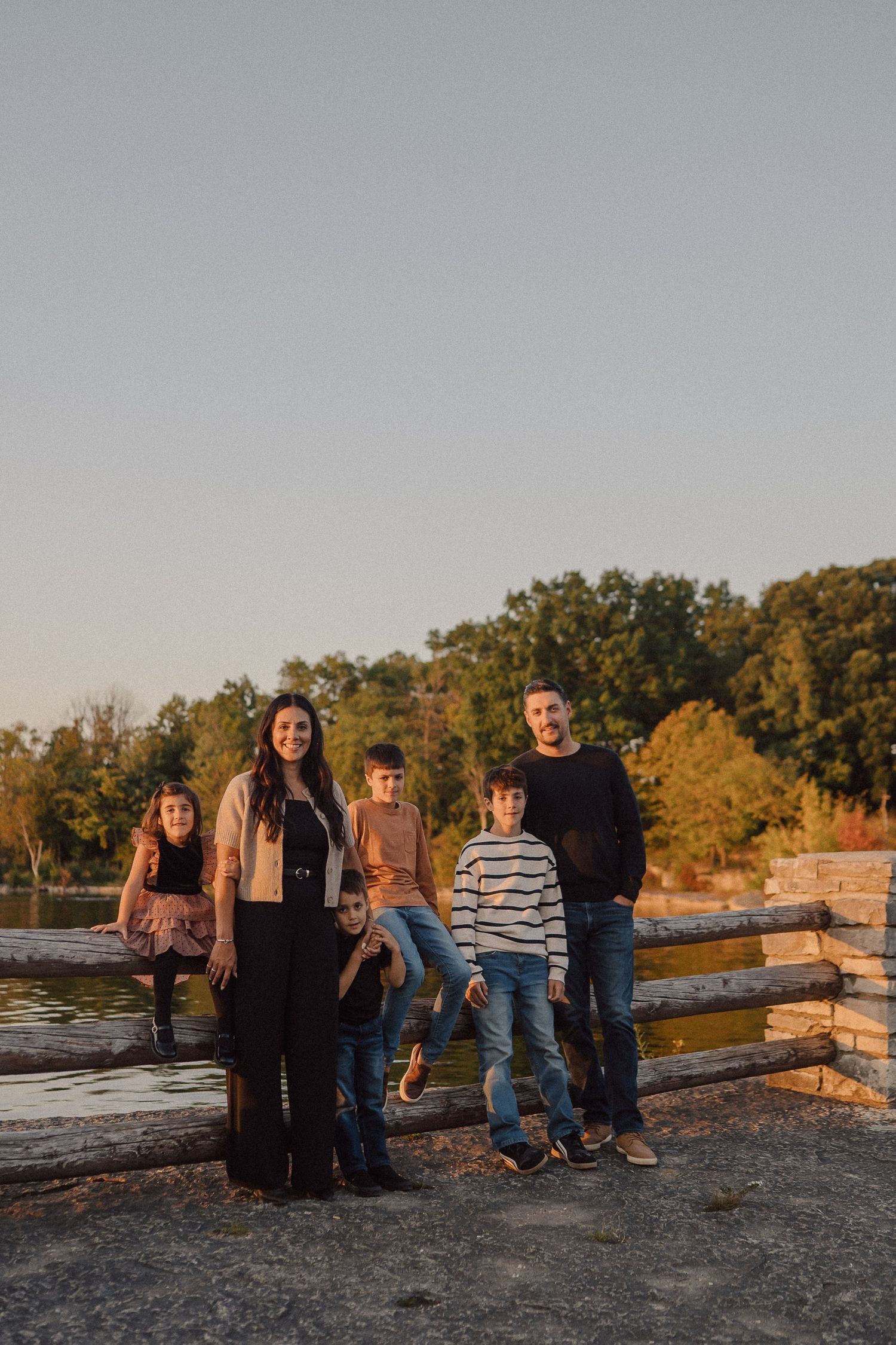 Family poses together on rocky terrain at sunset with golden autumn trees in the background.