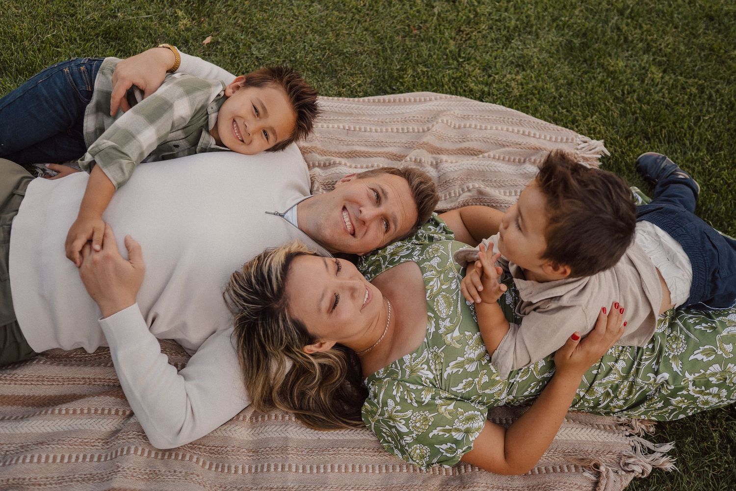 A family lies together on a cozy blanket in the grass during a relaxed outdoor photography session.