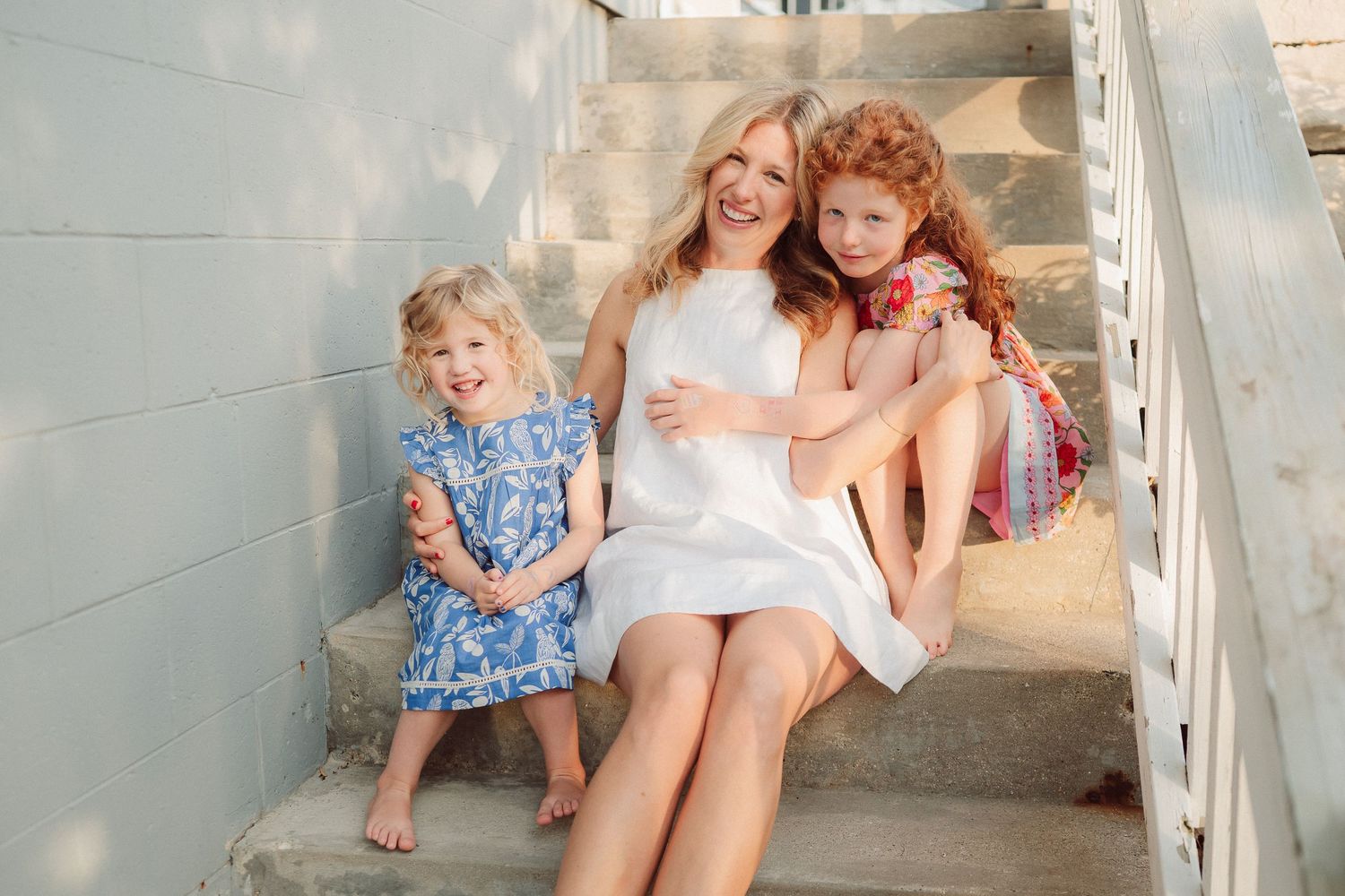 A group sits together on white porch steps during a sunny afternoon.
