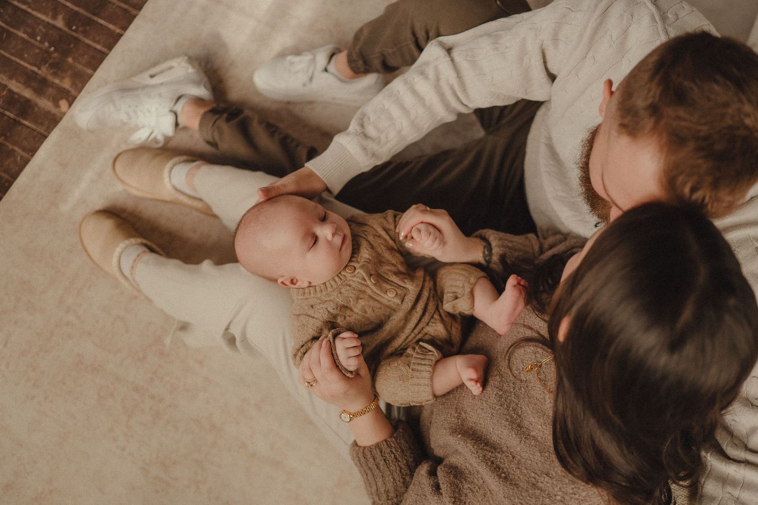 Tender moment between parent and baby lying together on white bedding in soft natural light.