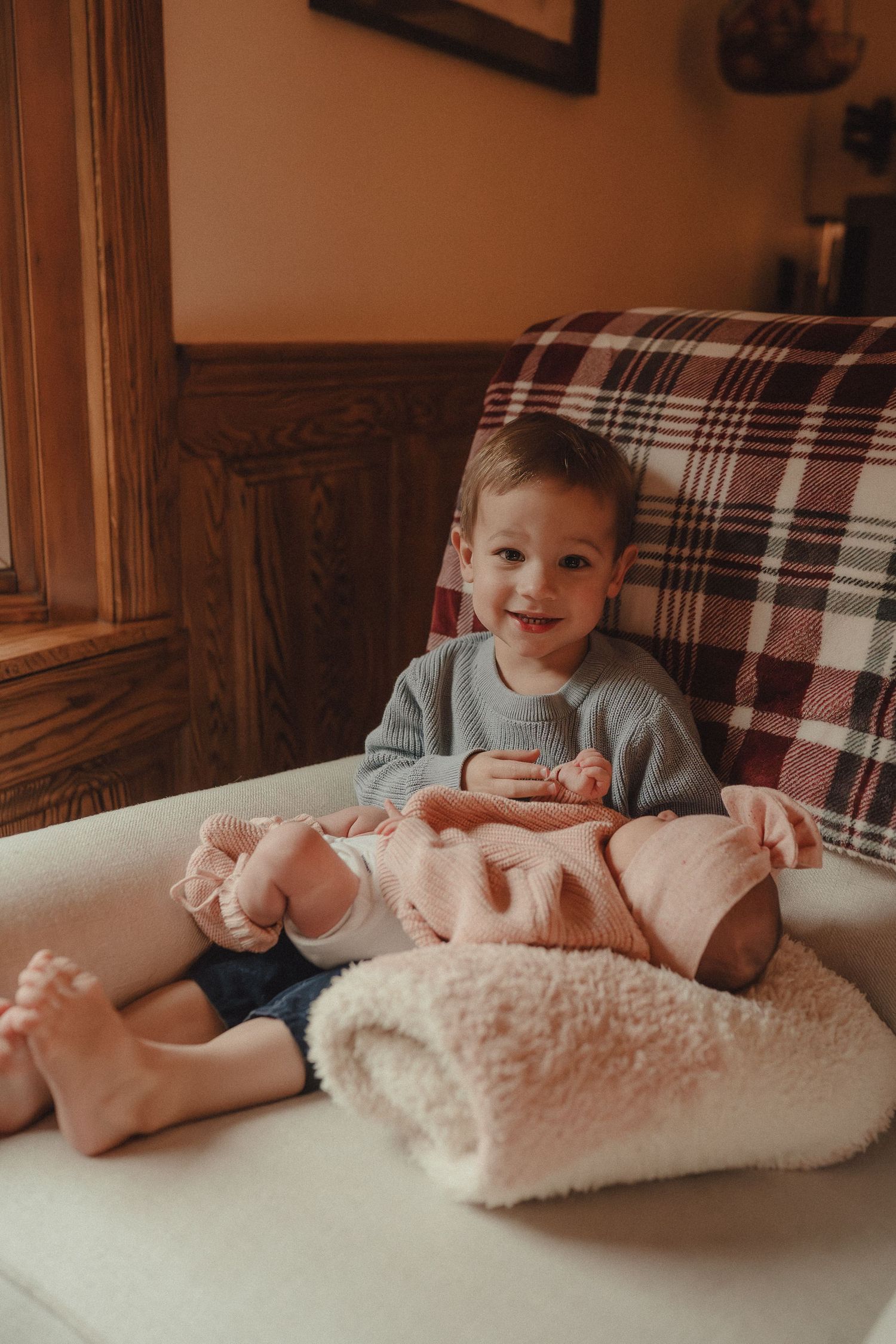 A small child relaxes on a plush white blanket near a window in a cozy home setting.
