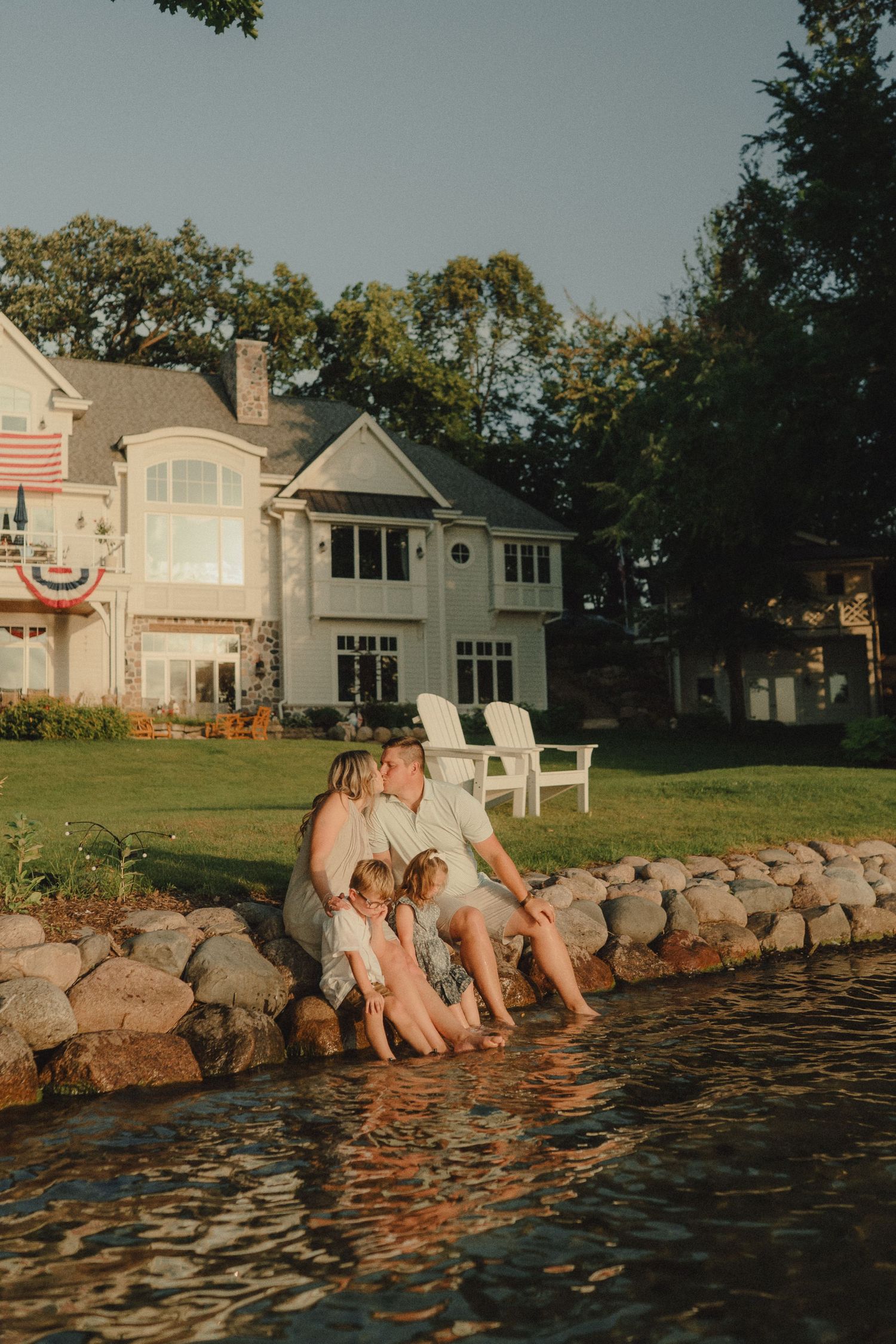 Family sitting together on stone edge dipping feet in lake at golden hour.