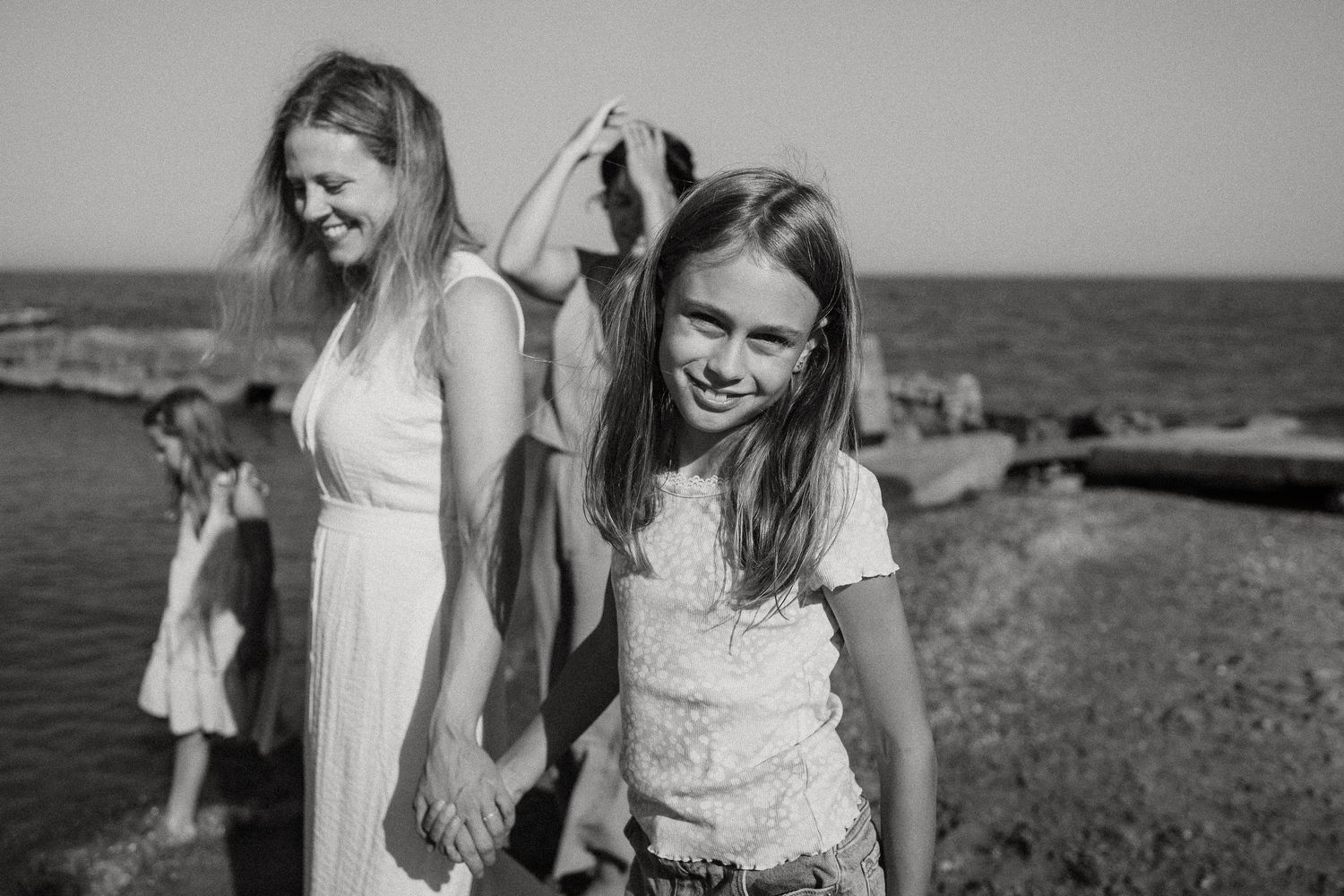 Black and white photo of two girls smiling by the ocean on a sunny day.