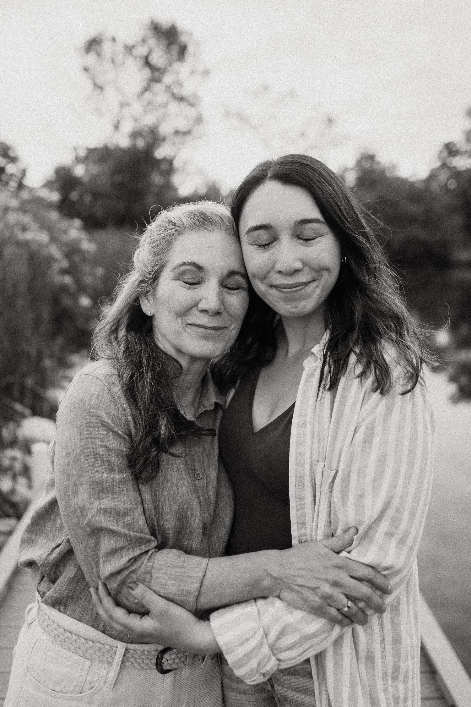 Black and white photo of two women sharing a warm embrace outdoors near water.