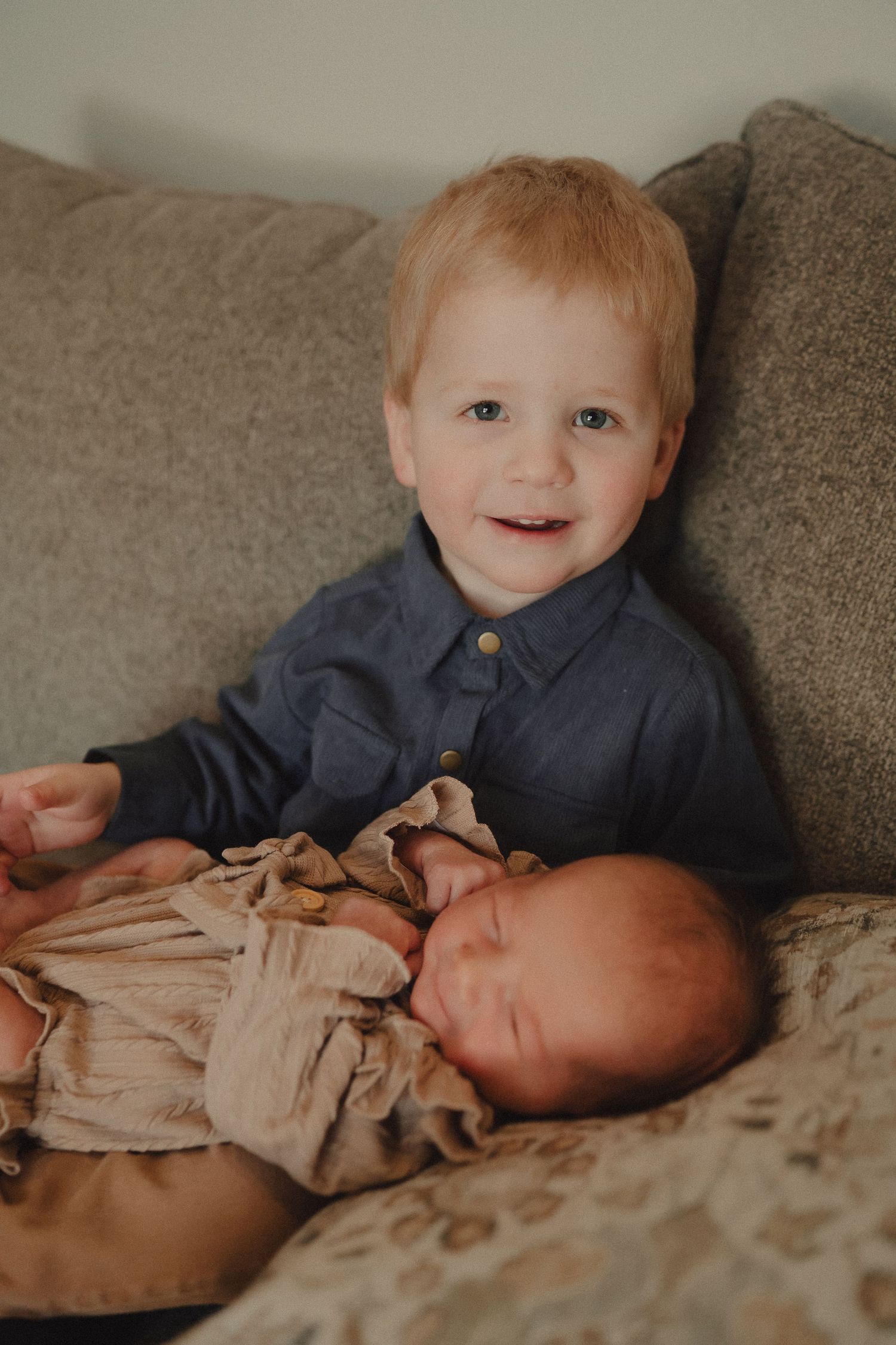 Two siblings share a sweet moment together on a gray couch.