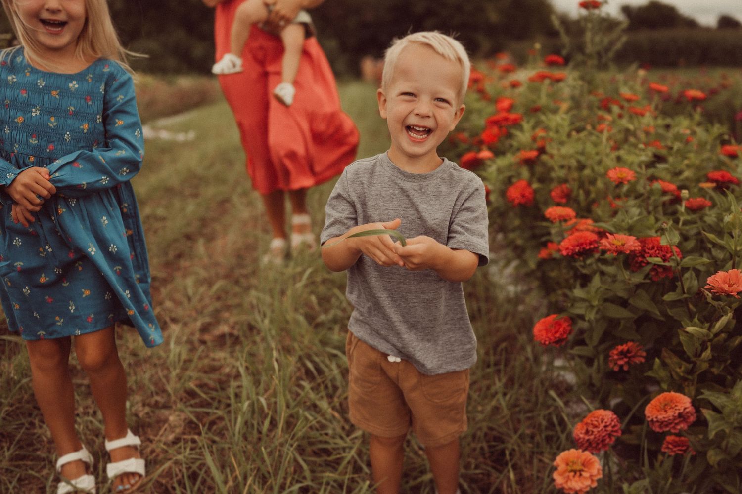 Children playing joyfully among blooming red flowers in a garden setting.