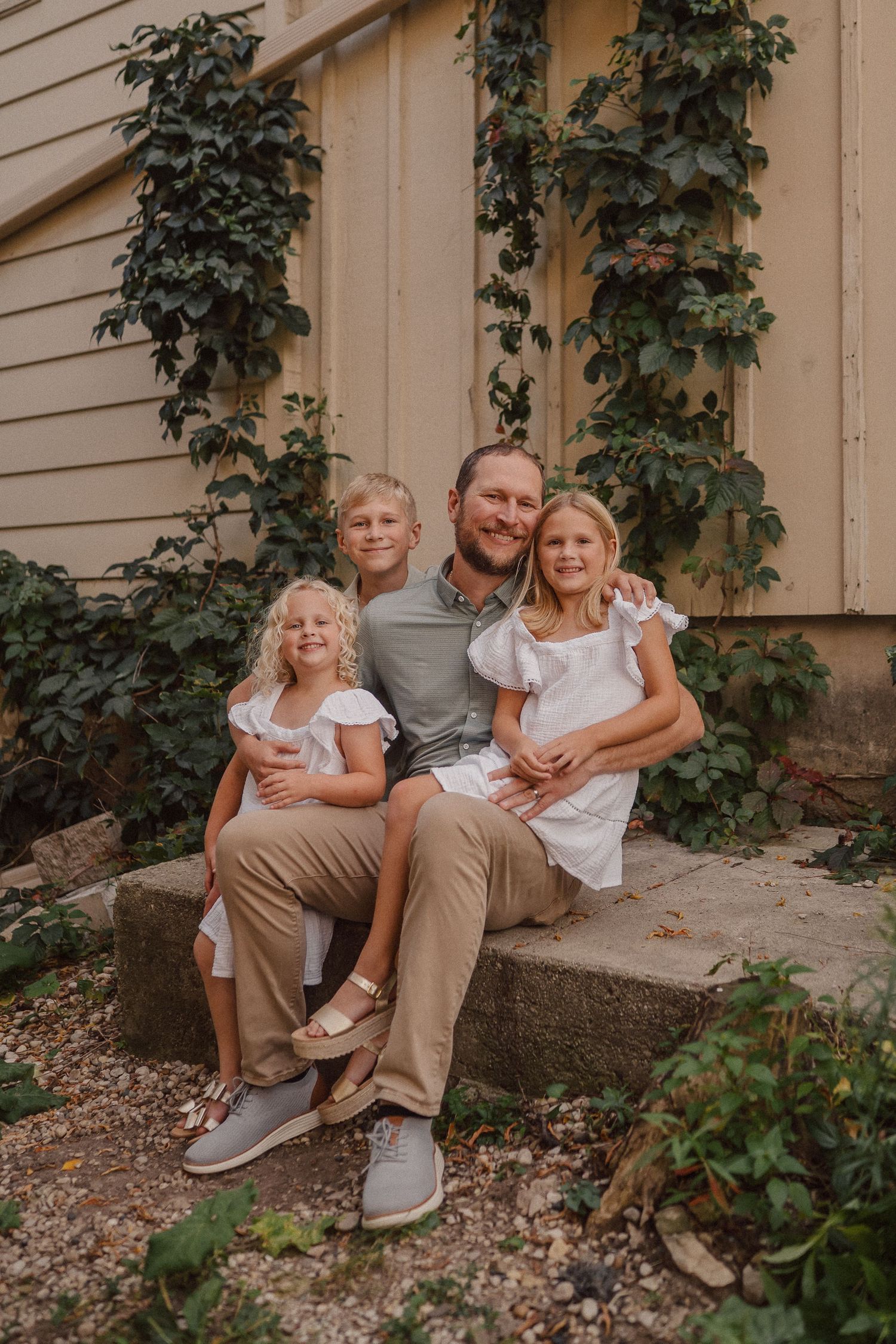 A family sits together on stone steps against a beige wall with climbing ivy vines.