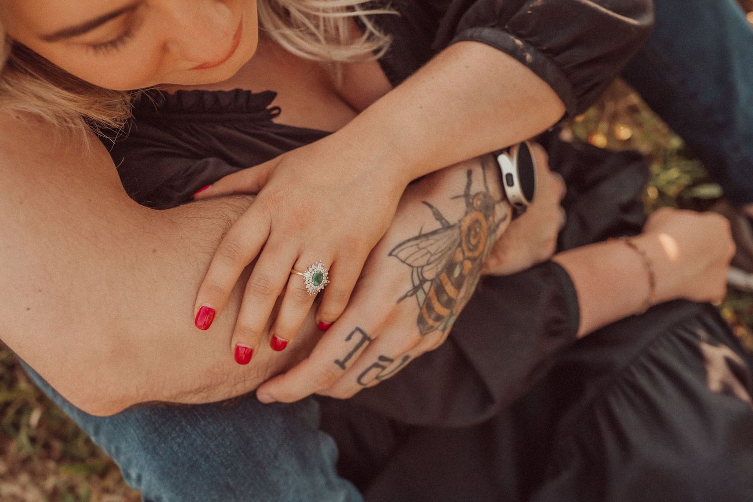 Close-up of hands with red nail polish and visible tattoos in an intimate moment.