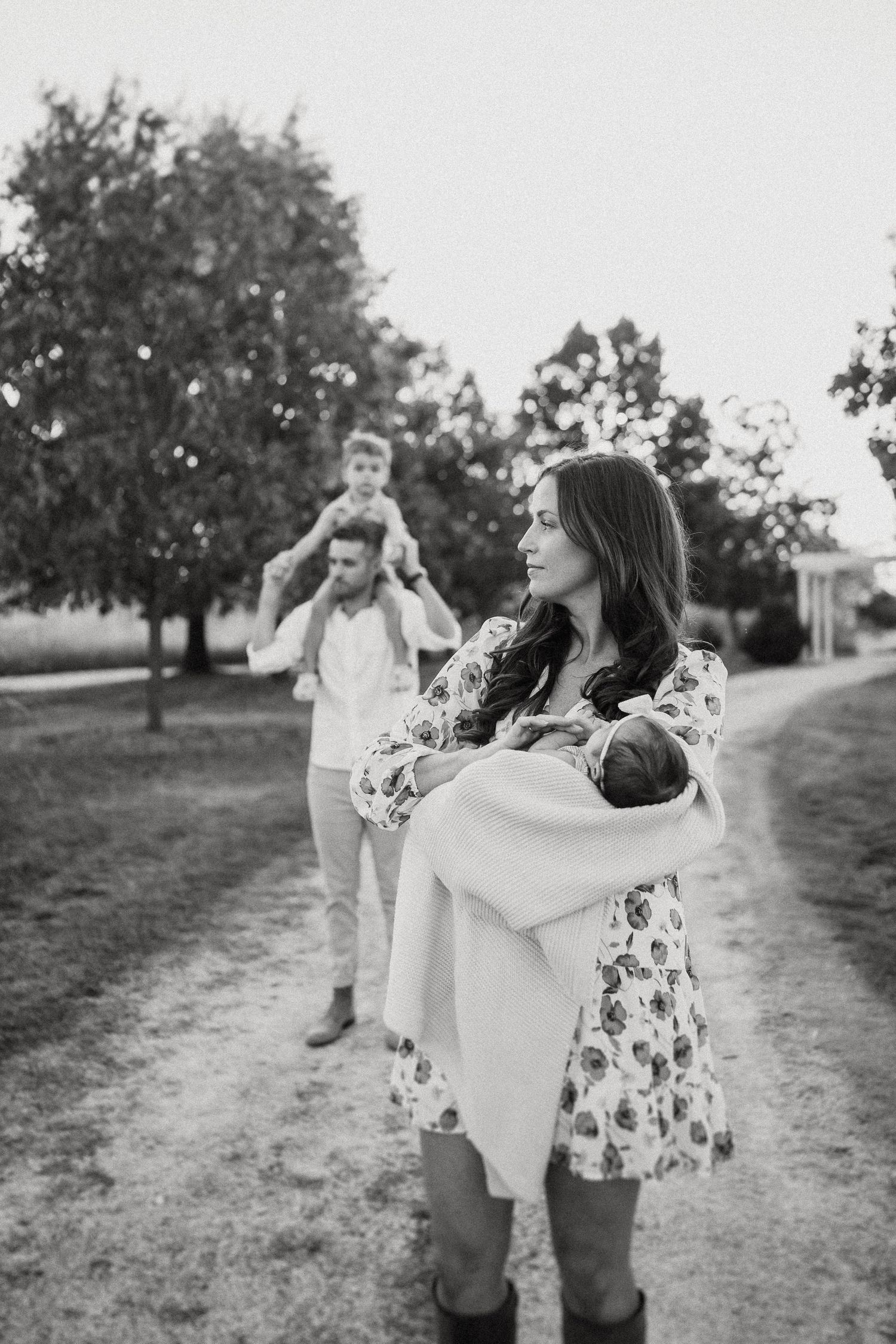 Black and white portrait of family enjoying outdoor moment on tree-lined path.