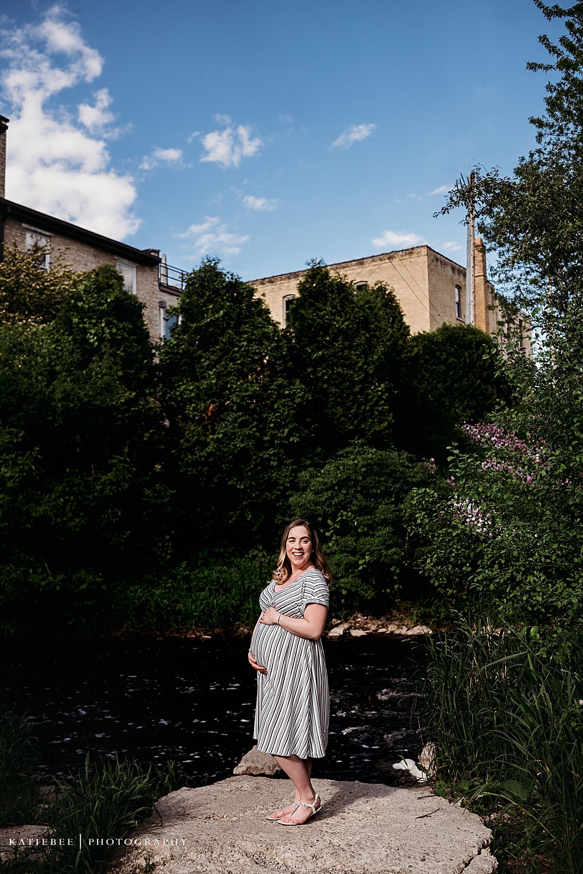 A maternity portrait against urban architecture and greenery on a sunny day.