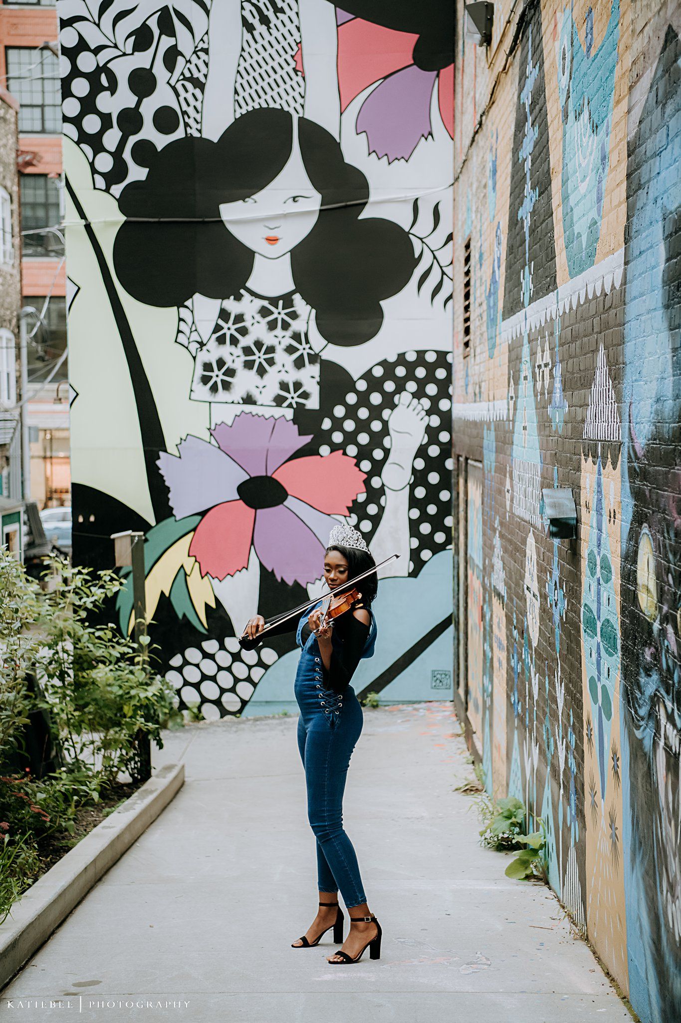 Violinist posing in front of whimsical black and white floral street art mural.