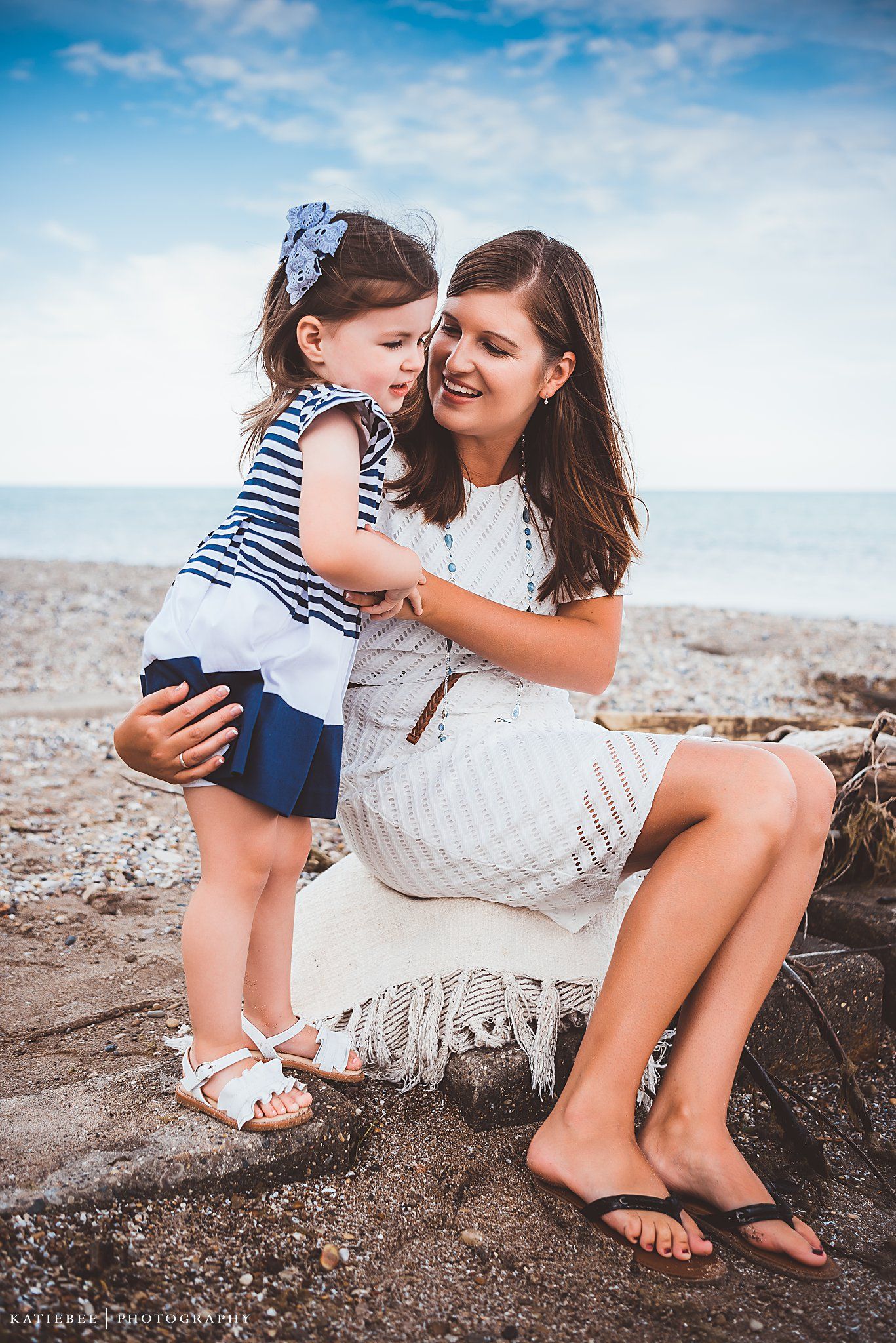 A tender moment shared between parent and child sitting on rocks by the ocean.
