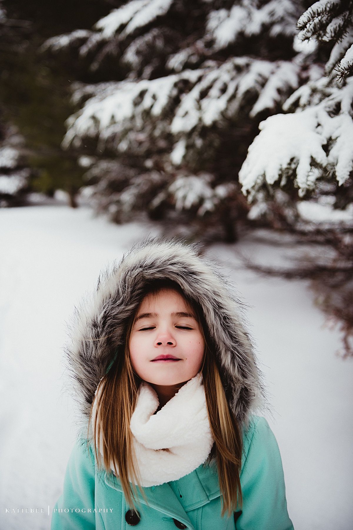Peaceful winter portrait featuring a mint coat and white scarf against snow-covered pine trees.
