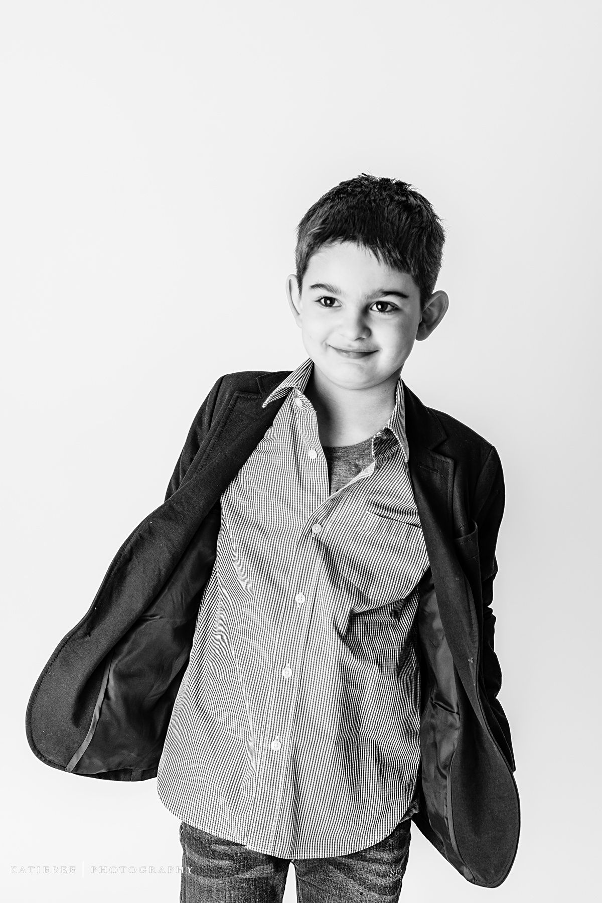 Black and white portrait of a young child in a blazer and button-down shirt striking a casual pose.