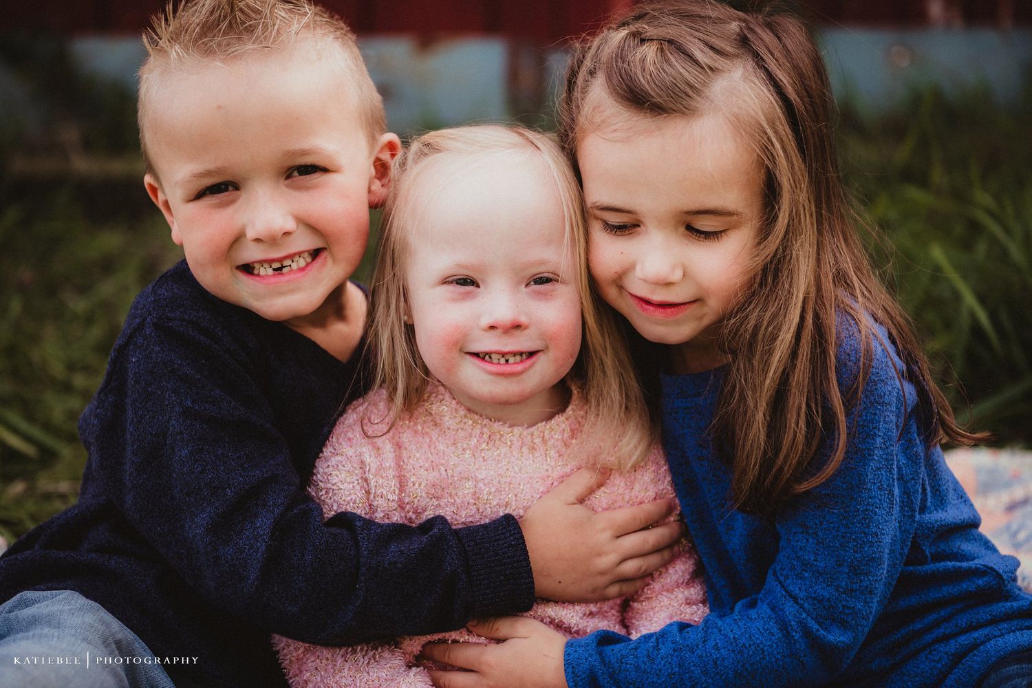 Three children huddle close together sharing joyful smiles outdoors.