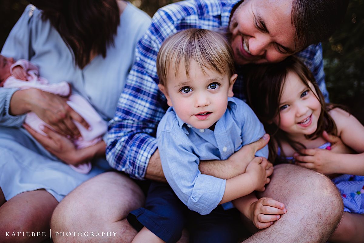 Family wearing coordinated blue outfits sits together outdoors during a casual photo session.