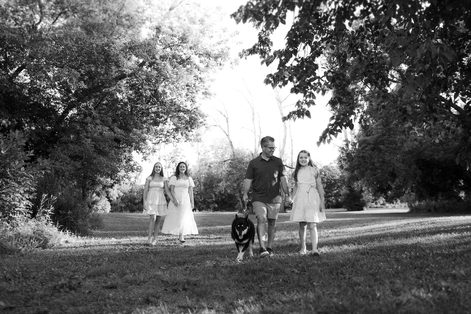 Black and white landscape photo showing people walking across a grassy hill under large trees.