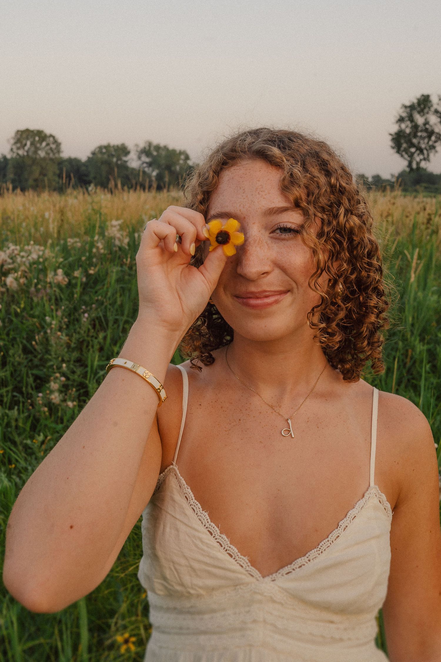 A playful portrait series in a sunlit field with yellow flowers and a cream-colored dress.