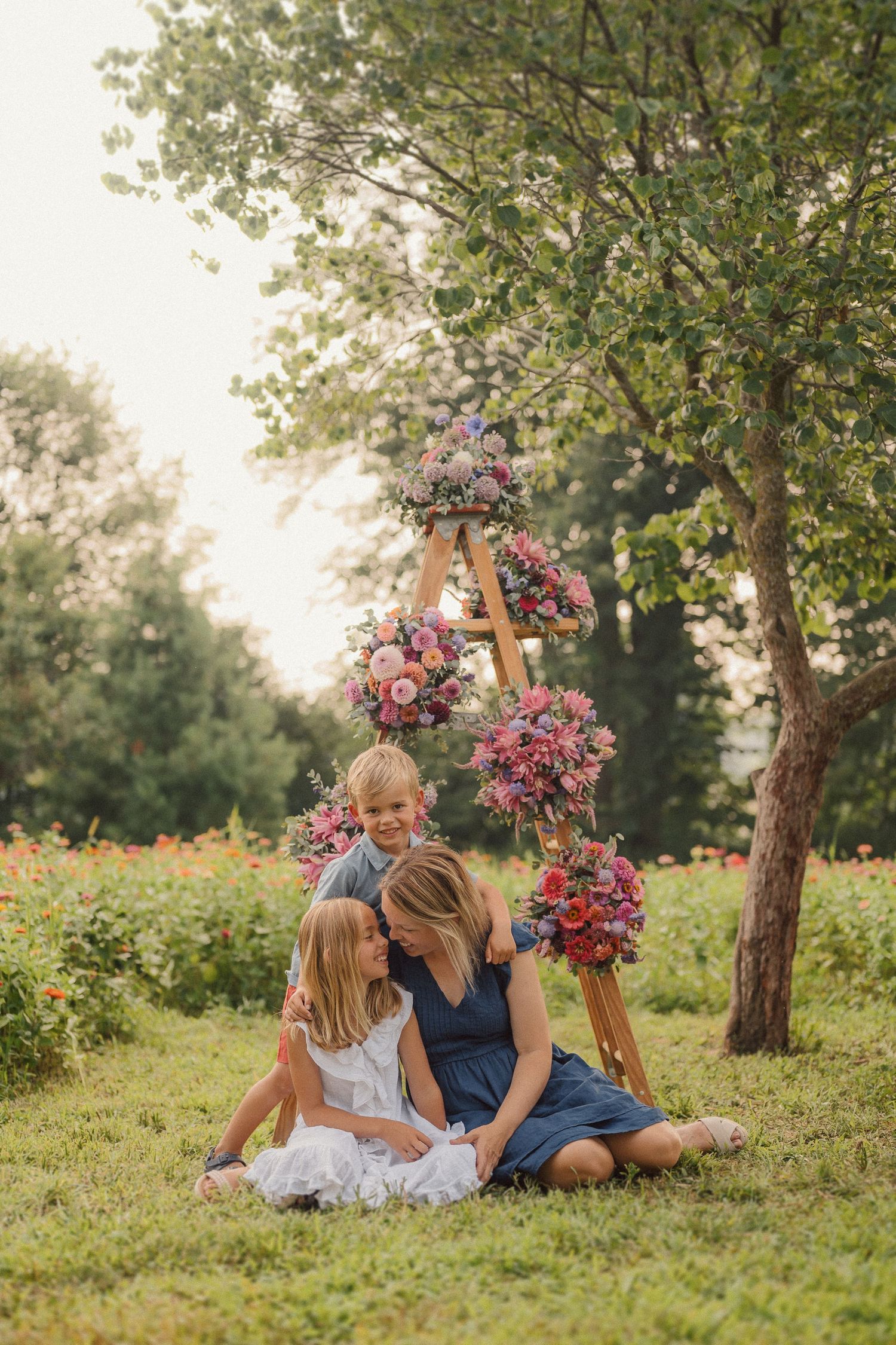 Couple sitting on grassy hill together with pink and purple floral arrangements in a romantic outdoor setting.